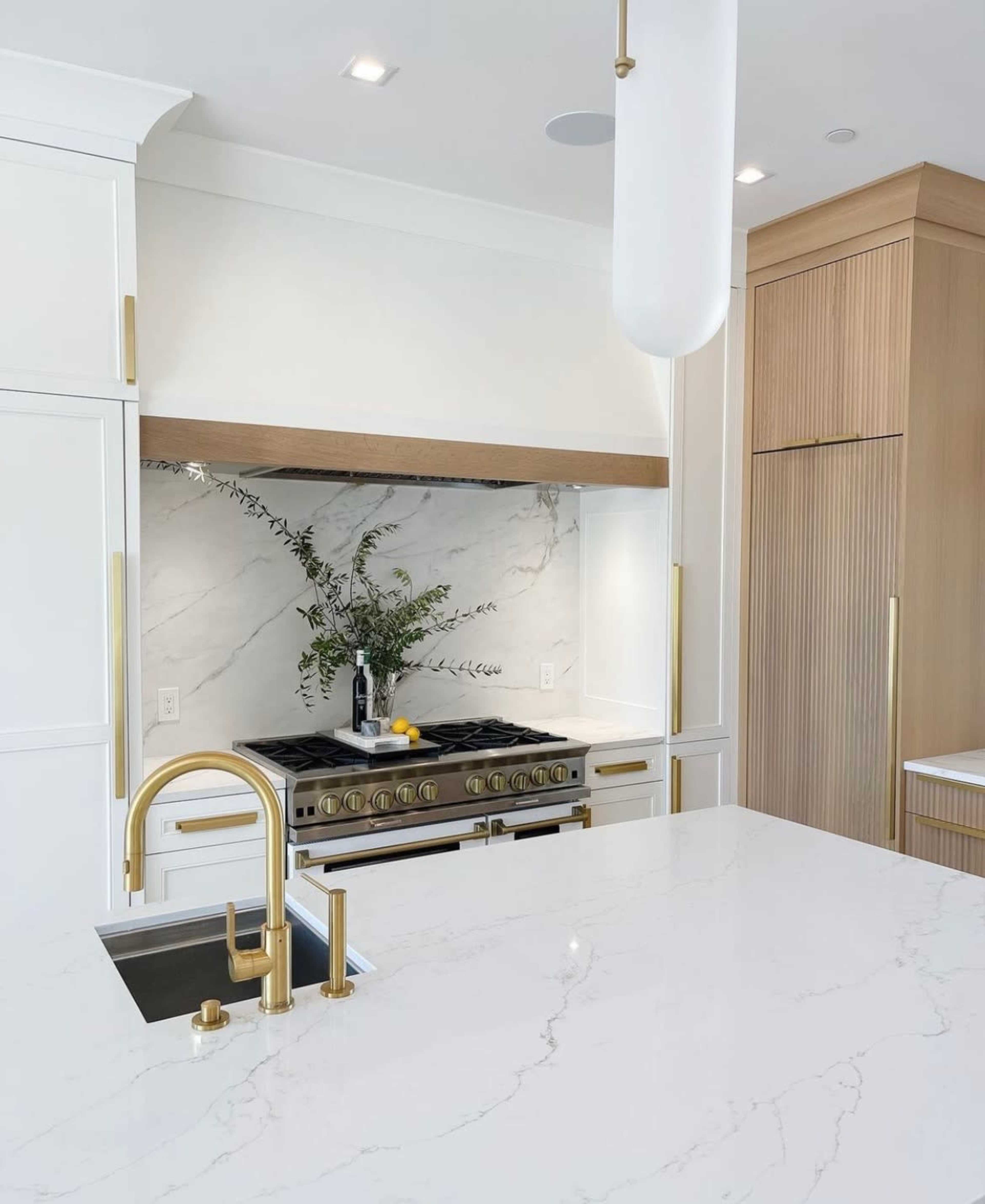 A modern kitchen features a marble backsplash, stainless steel stove, and a large white island with a gold faucet.