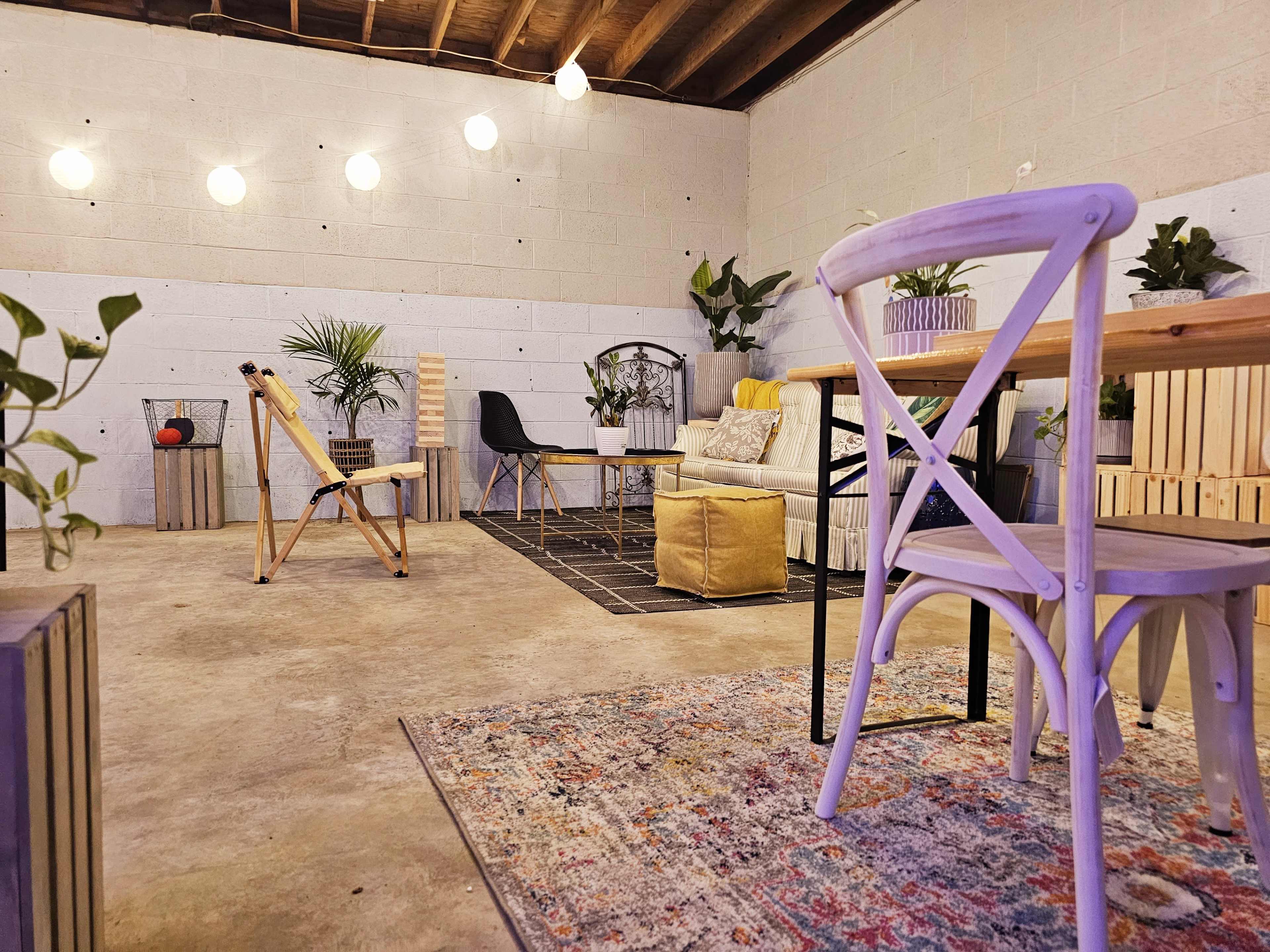 A cozy interior space features wooden furniture, plants, and decorative lighting against a concrete wall.