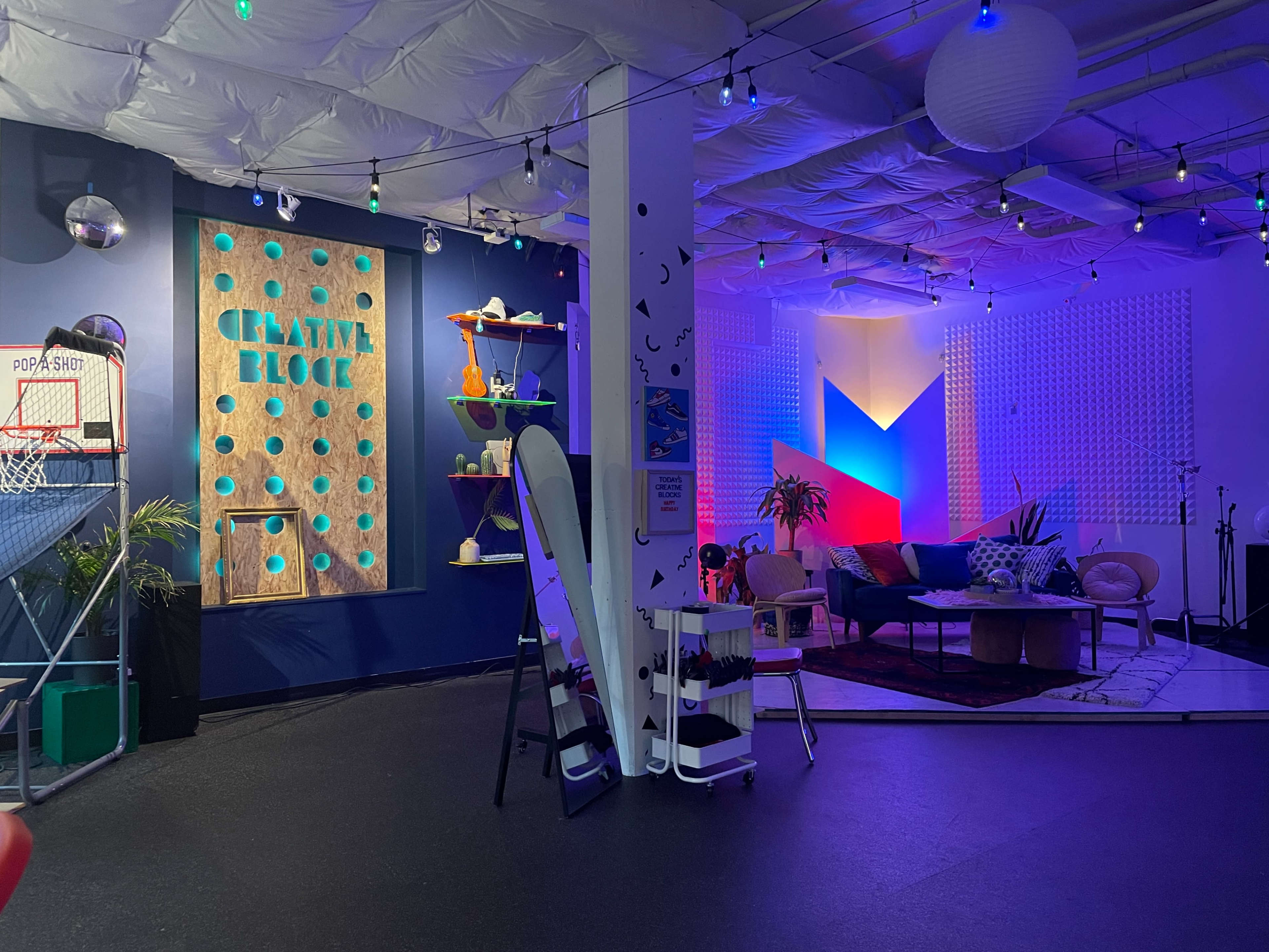 A vibrant creative space featuring a basketball hoop, colorful decor, and a lounge area with couches and art hanging on the walls.