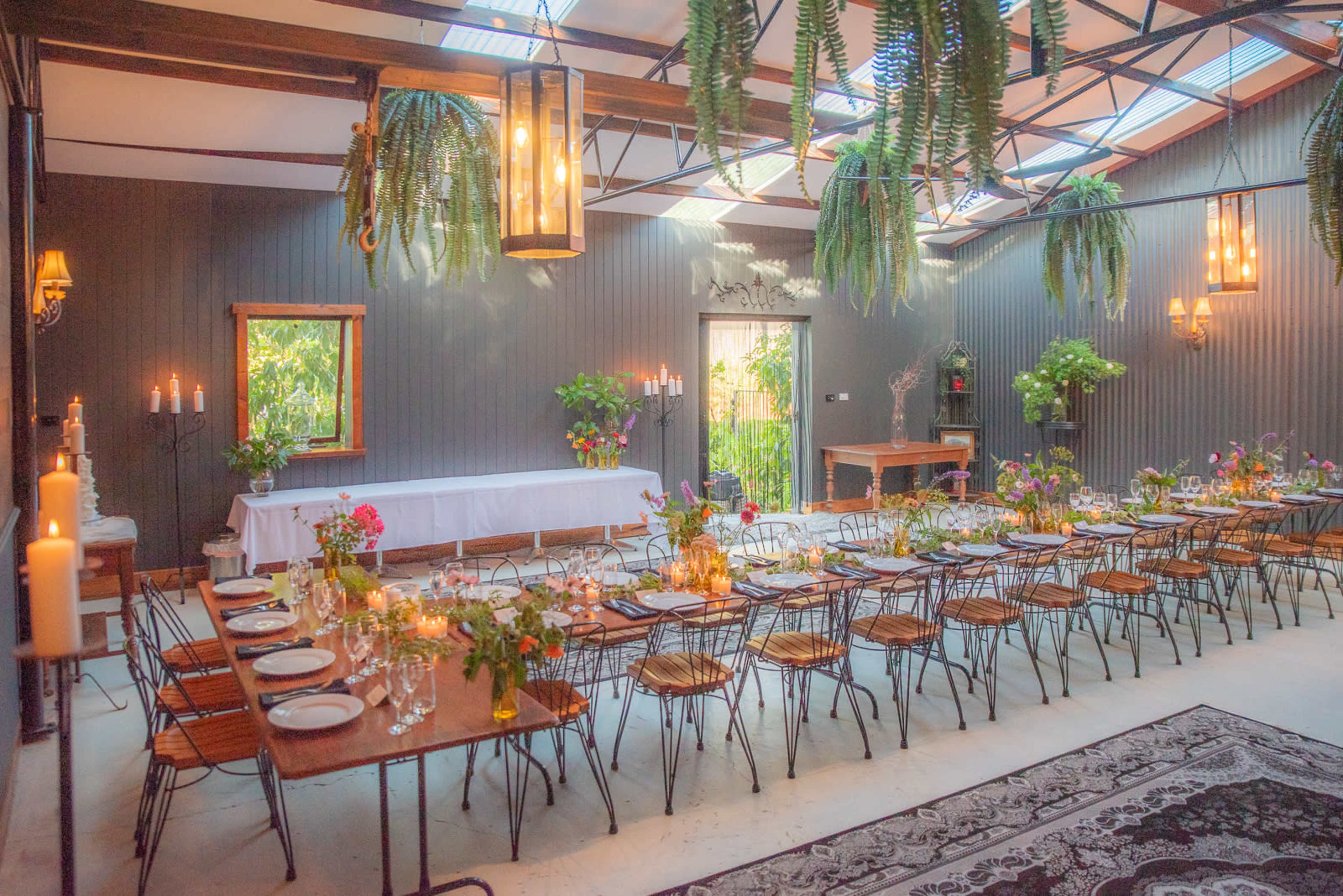 An elegantly arranged dining area with a long table set for a meal, surrounded by greenery and decorative lighting.