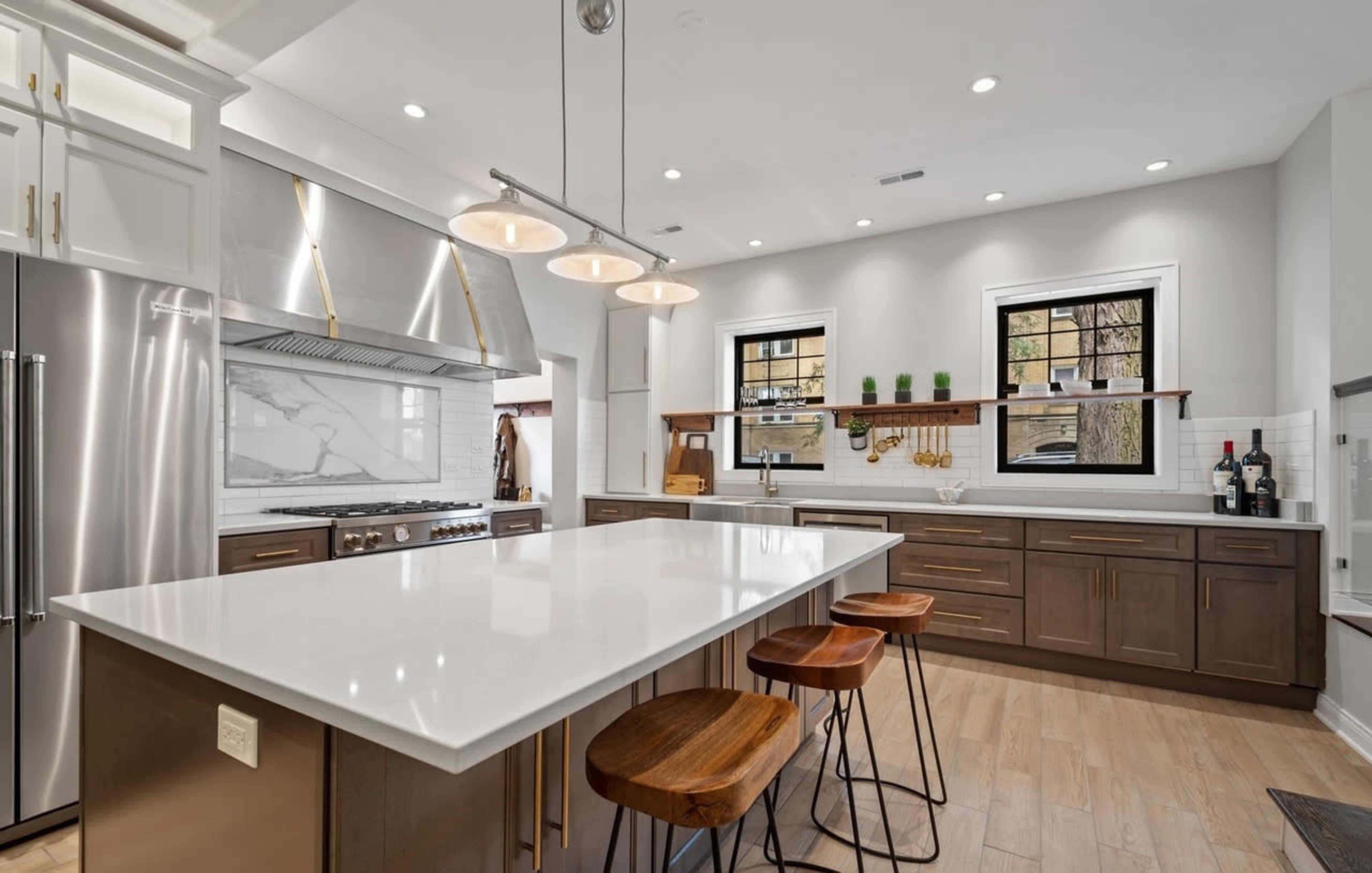 A modern kitchen features a large island with wooden stools, stainless steel appliances, and a marble backsplash.