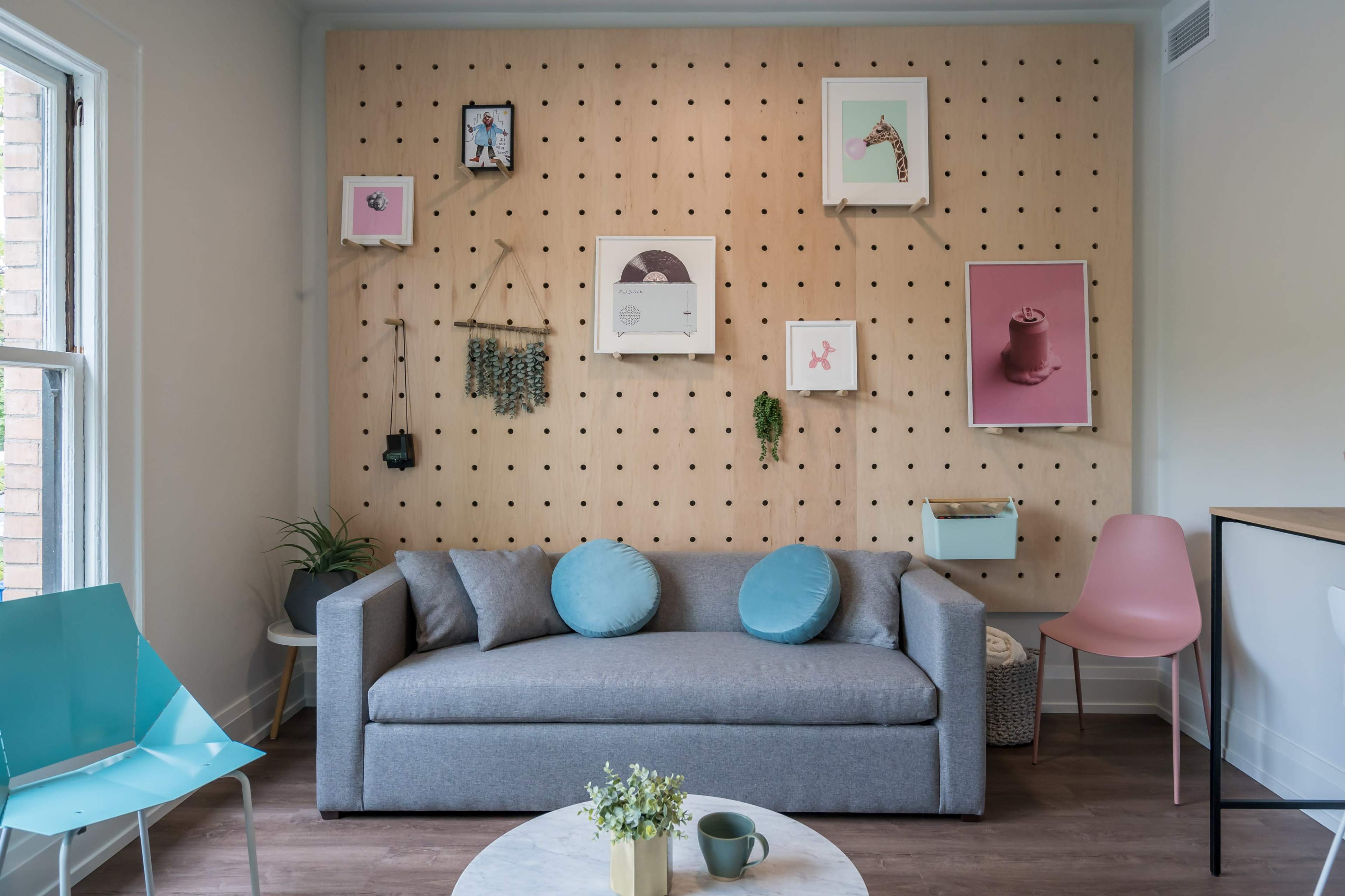 A modern living room with a gray sofa adorned with blue cushions, set against a pegboard wall displaying various framed artworks.
