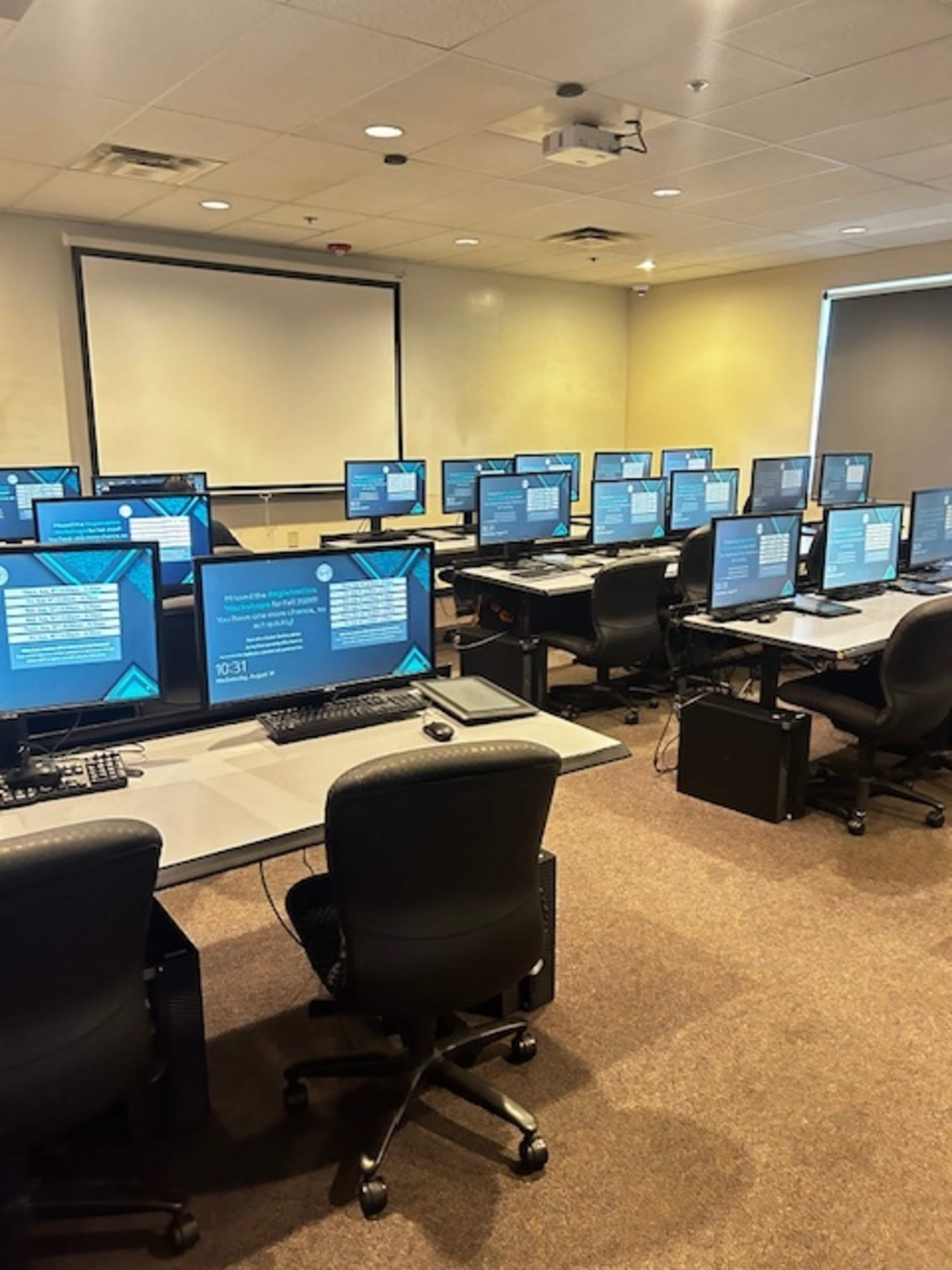 A classroom is filled with rows of computers set up on desks, each displaying the same instructional screen.