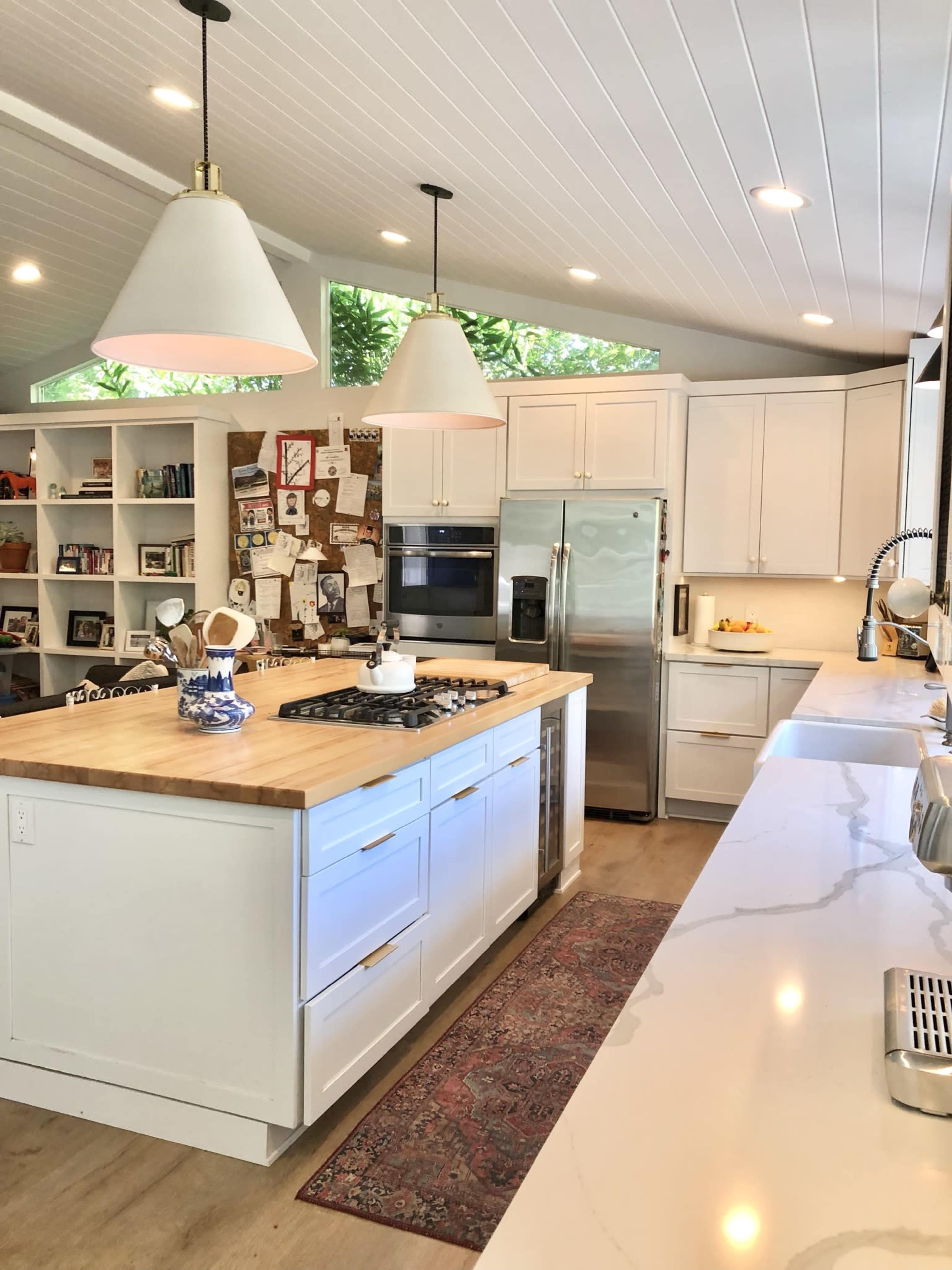 A modern kitchen featuring a central island with a wooden countertop, white cabinetry, stainless steel appliances, and pendant lighting.