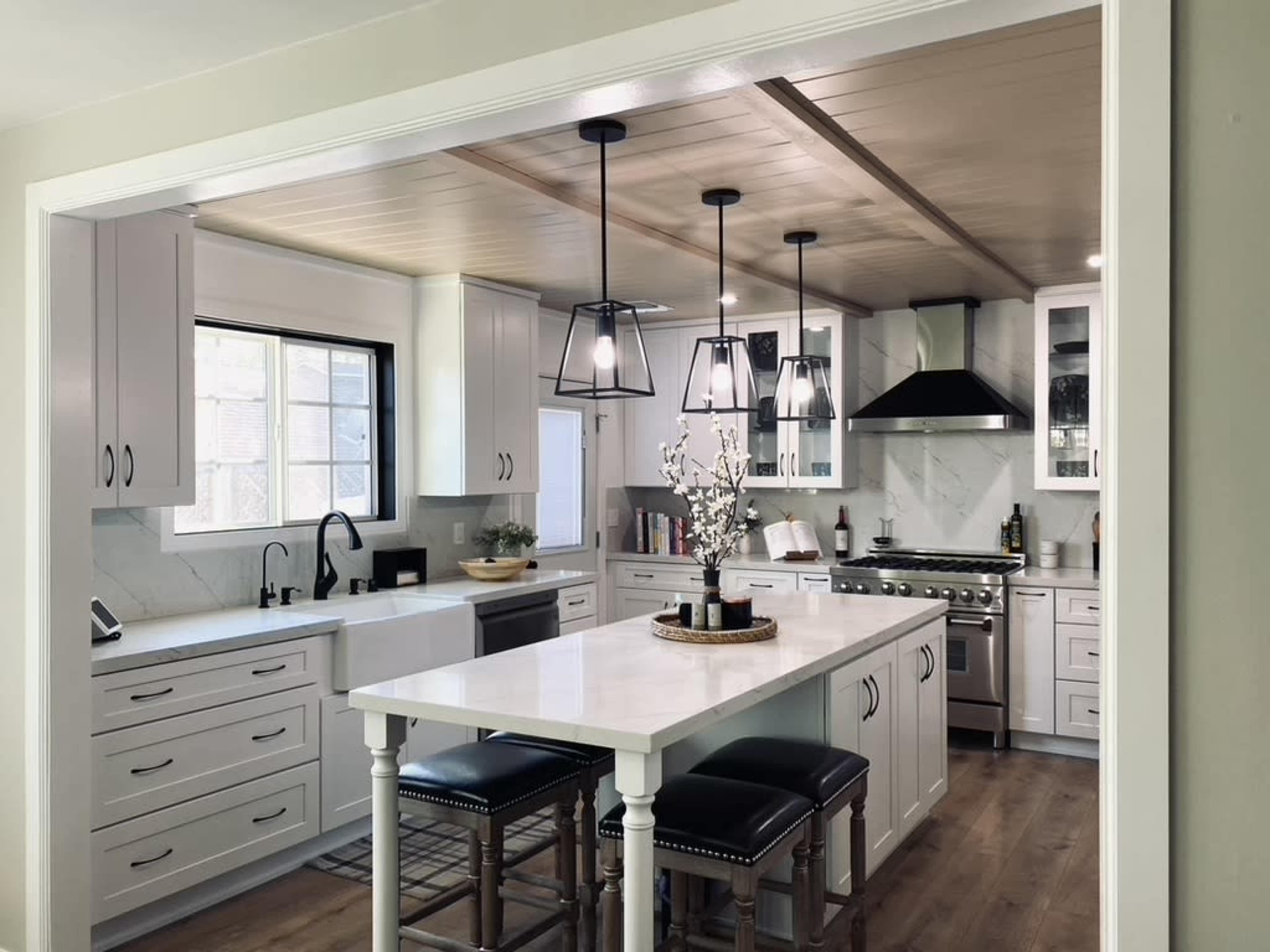 A modern kitchen features white cabinetry, a central island with seating, and pendant lighting above.