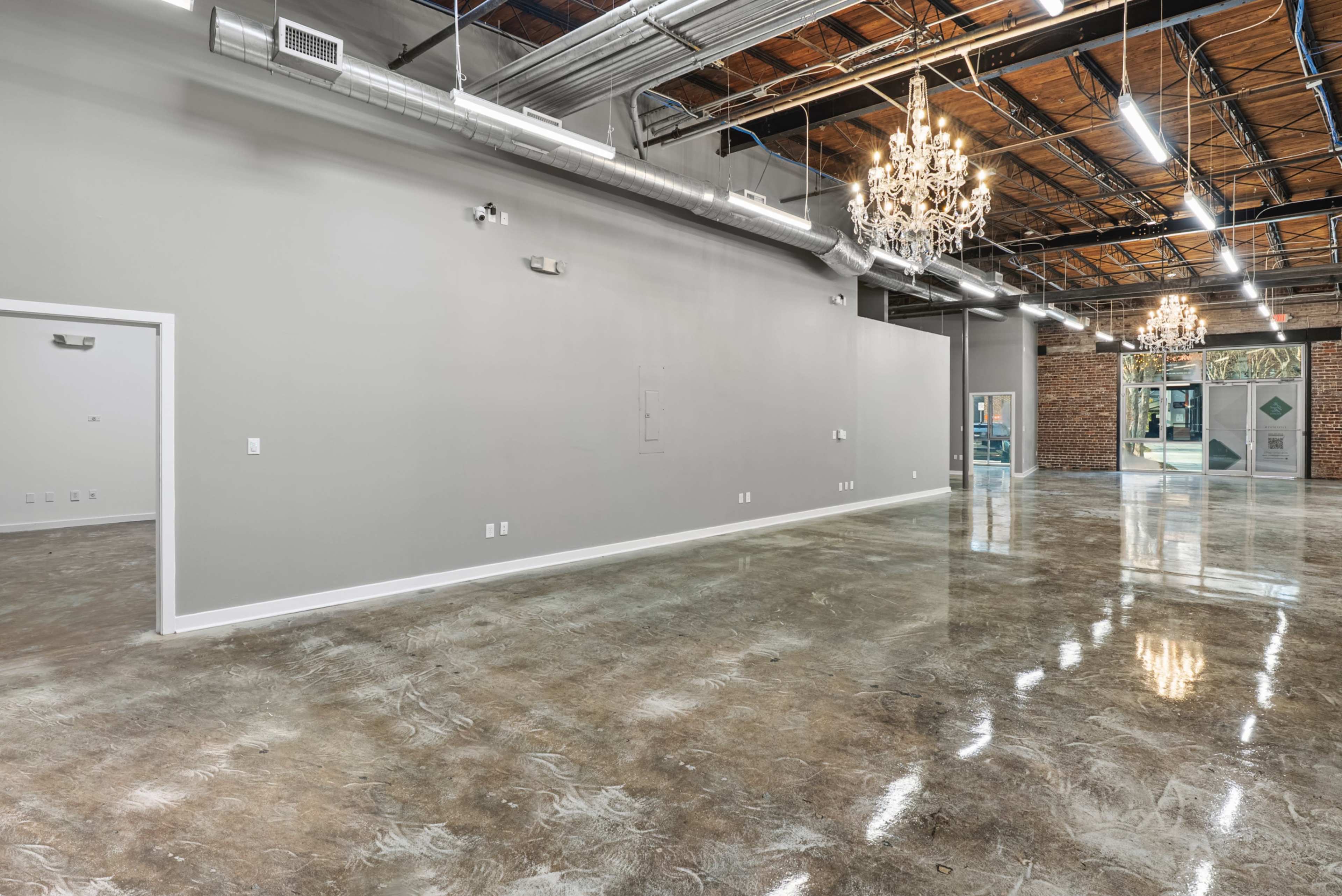 The image showcases a spacious, empty interior with polished concrete floors, high ceilings, and several chandeliers hanging from the ceiling.