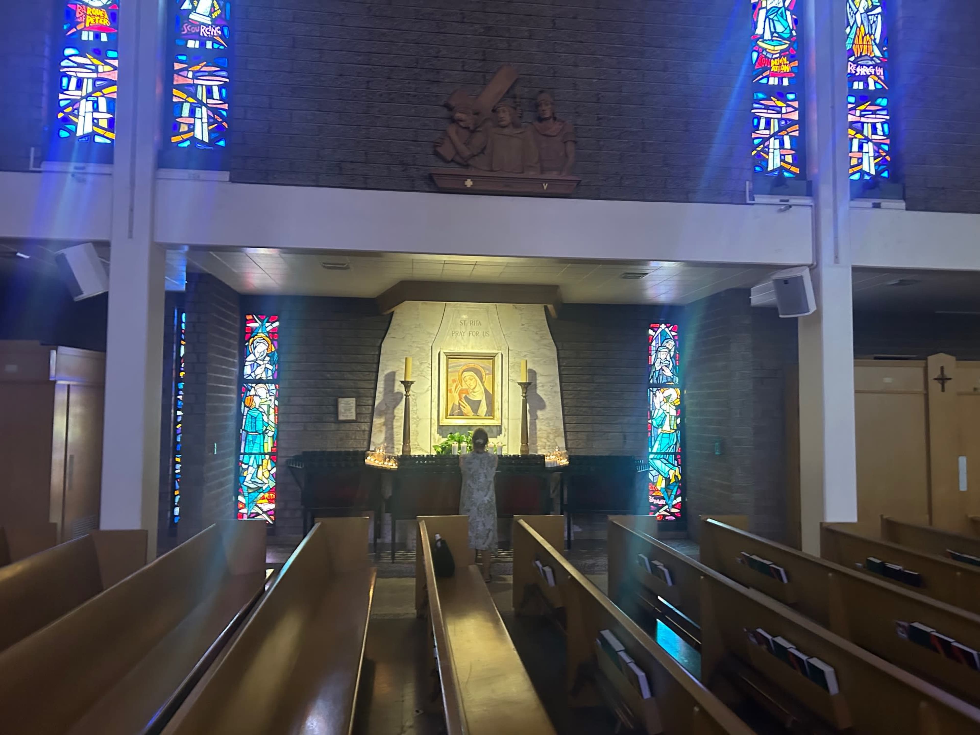 The image shows the interior of a church with a central altar illuminated by stained glass windows and wooden pews arranged in rows.