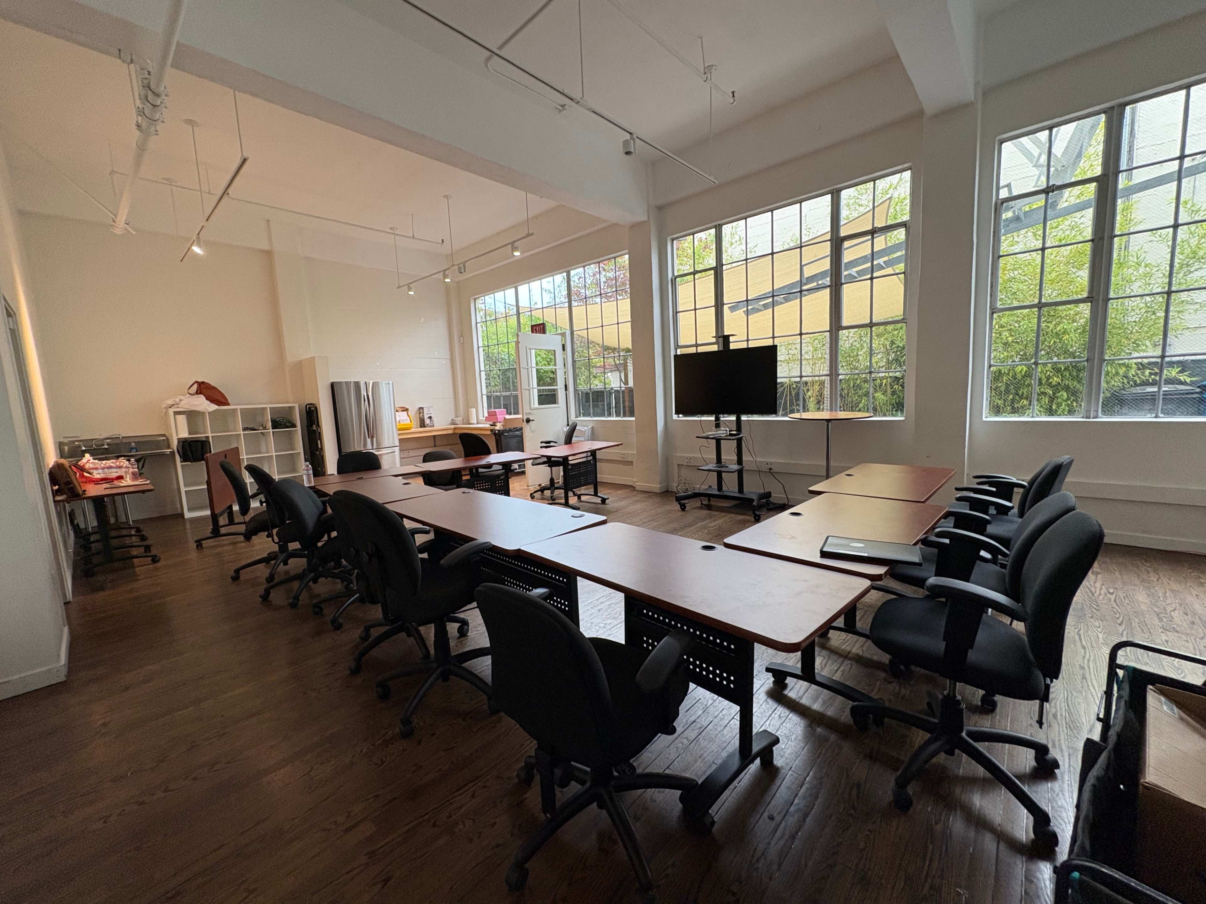 The image shows a spacious conference room with a long table, black chairs, a large screen, and large windows allowing natural light to enter.