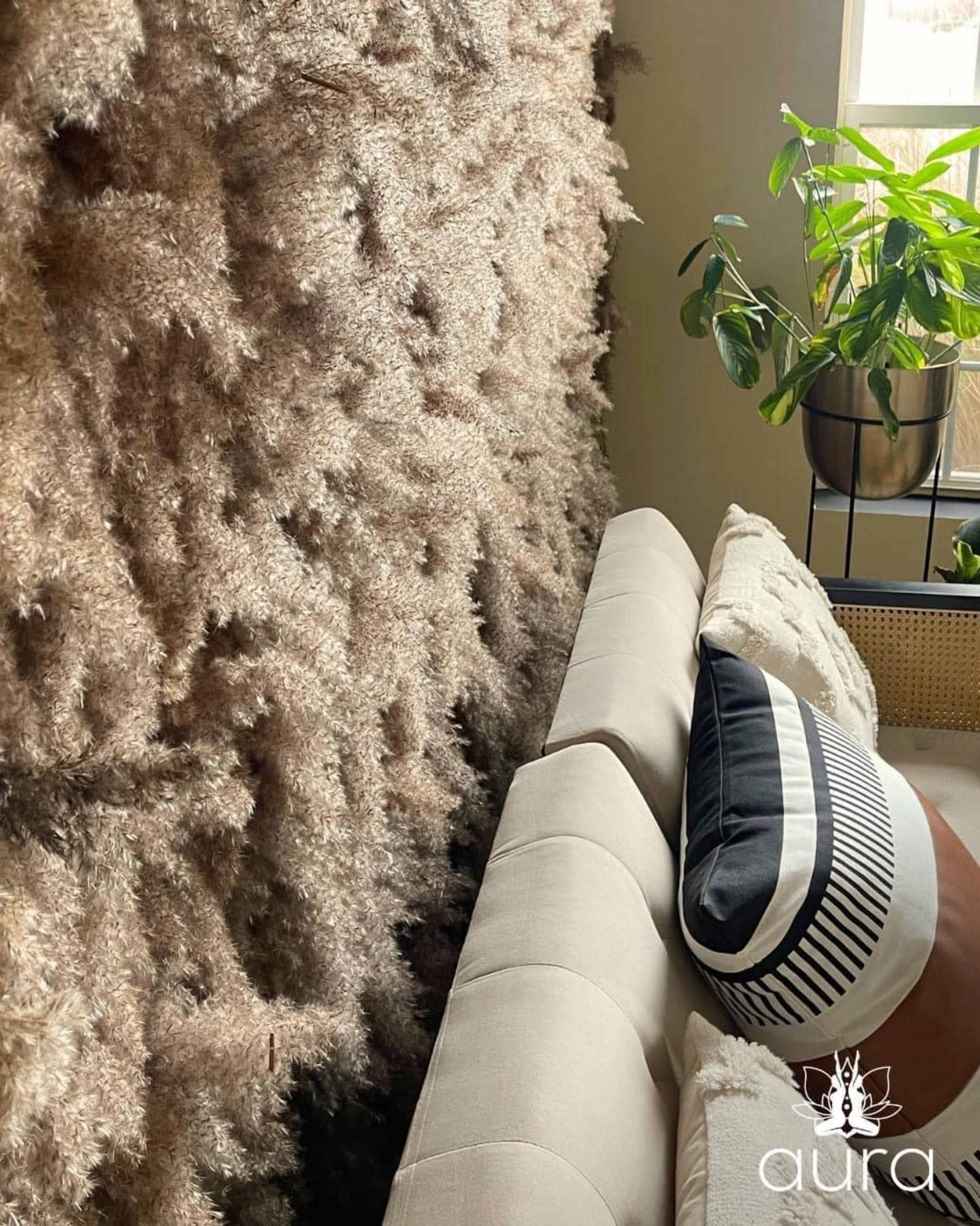 A light-colored couch is positioned against a textured wall of dried foliage, with a decorative throw pillow placed at one end.