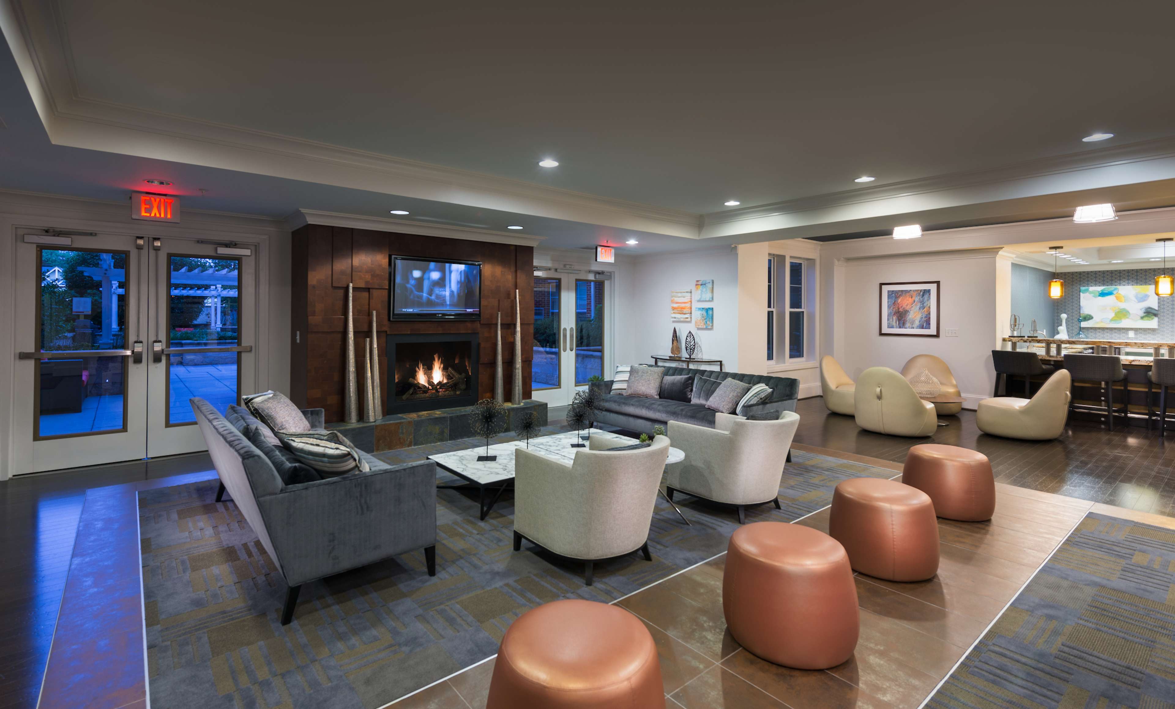 A modern lounge area featuring comfortable seating, a fireplace, and a bar in the background.