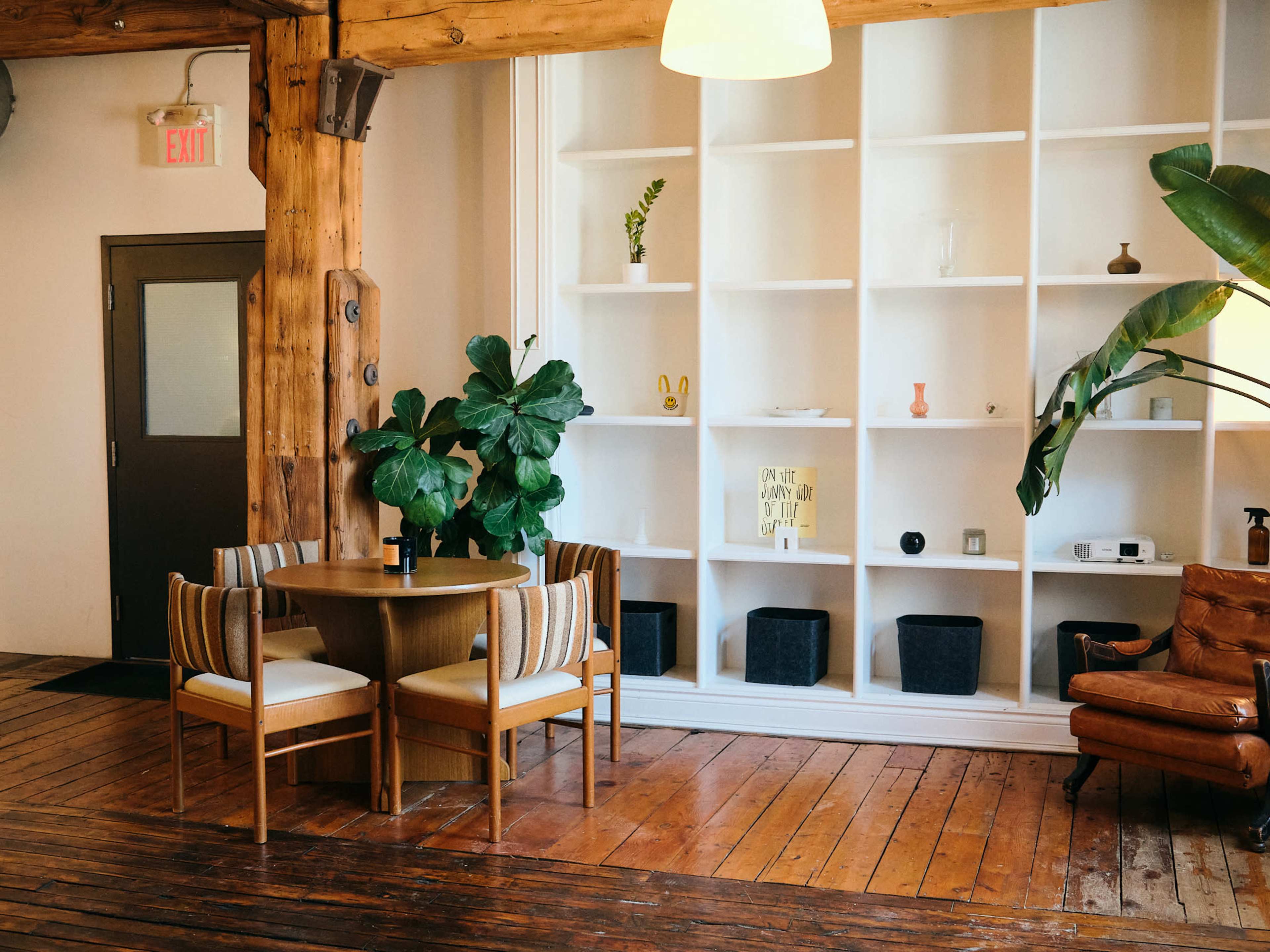 A cozy seating area features a round wooden table surrounded by four chairs, with a large shelf displaying decorative items in the background.