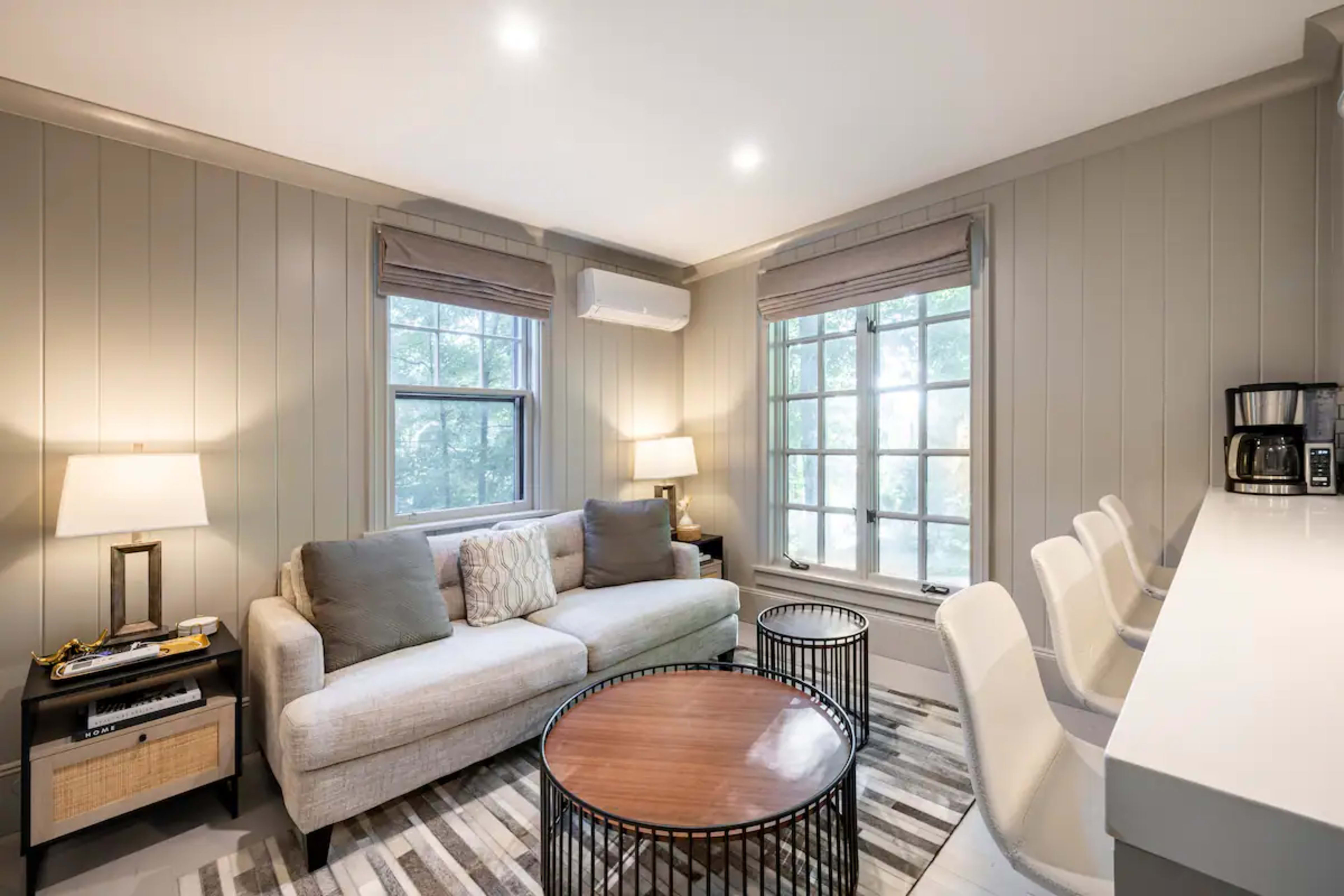 A living room with a light-colored sofa, a round coffee table, and large windows that provide natural light.