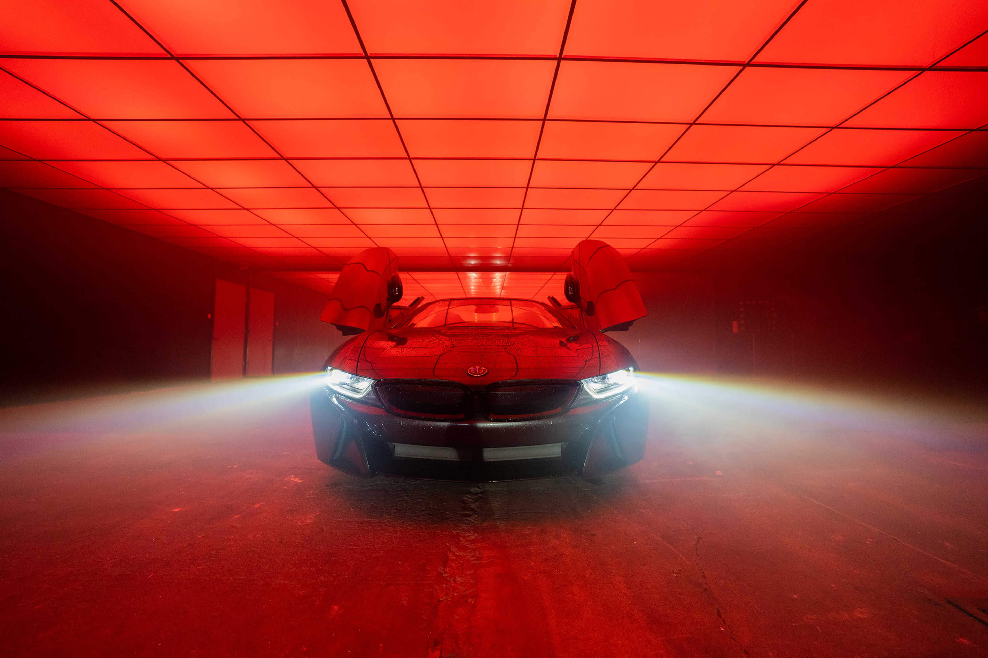 A sleek car with its doors open is illuminated by bright red lights under a grid ceiling.
