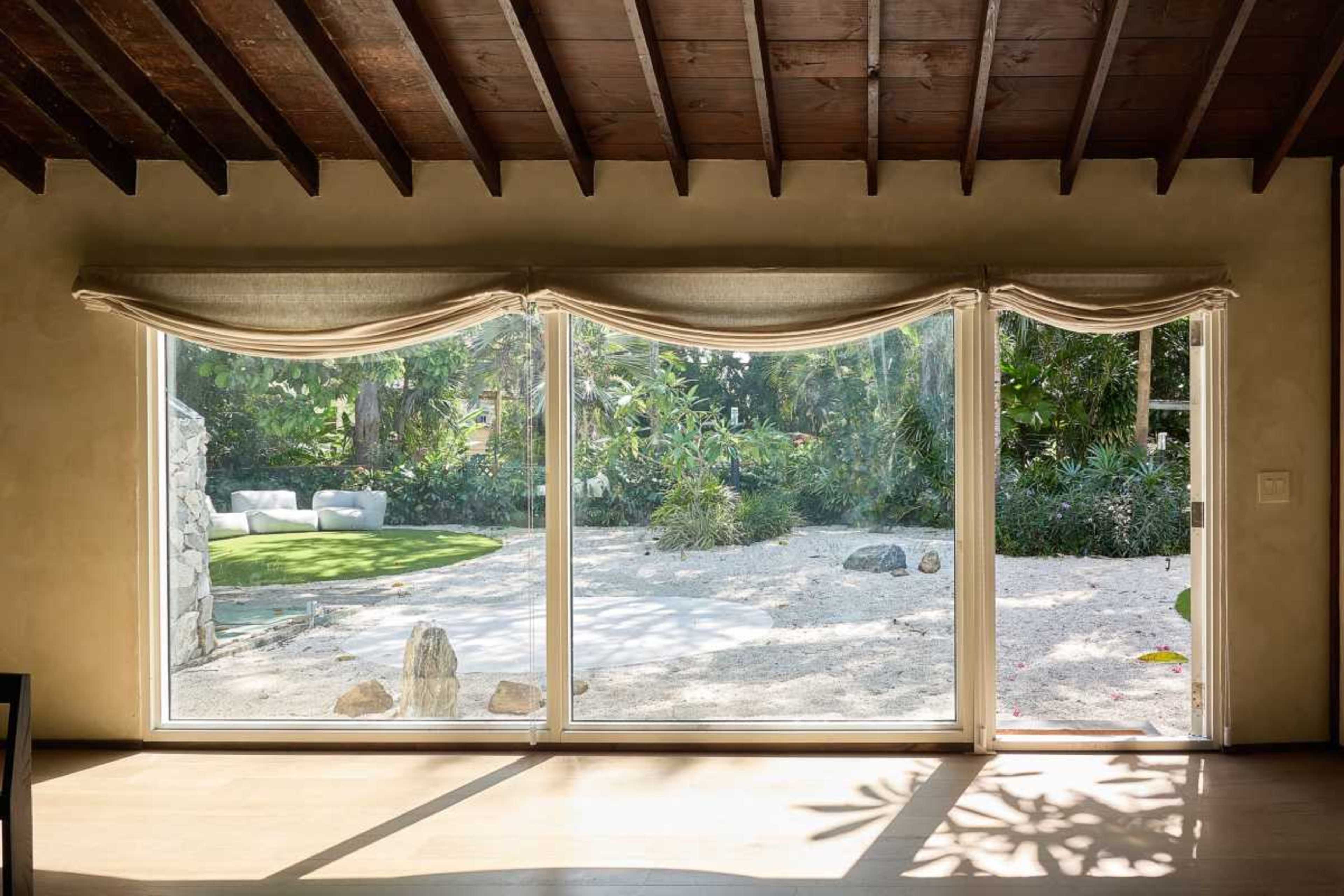 The image shows large sliding glass doors opening to a garden featuring a grassy area and various plants.
