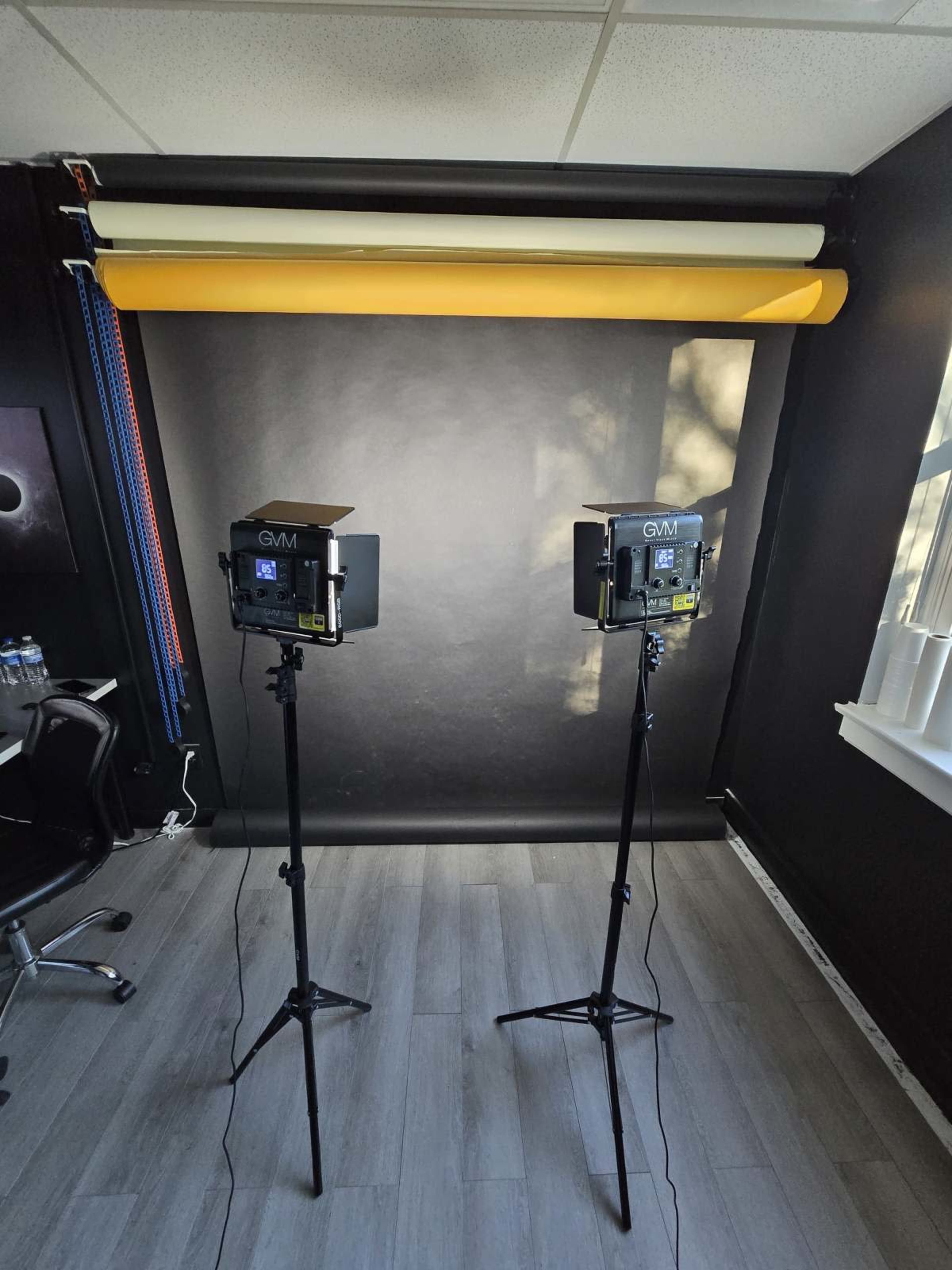 A photography setup with two lights on tripods facing a black backdrop and a yellow roll of paper above them.