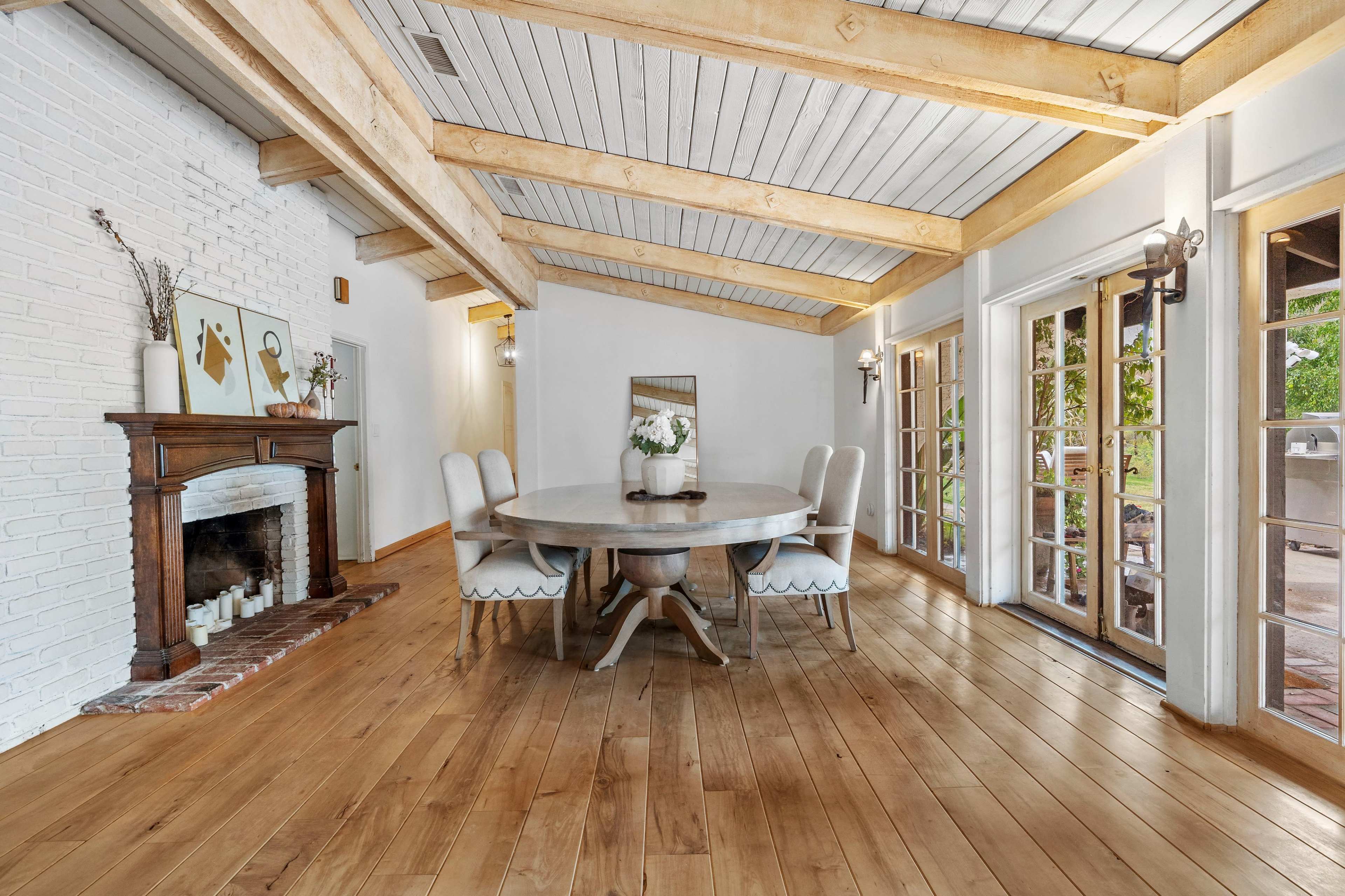 A dining area features a circular table surrounded by upholstered chairs, with exposed beam ceilings and a fireplace along one wall.