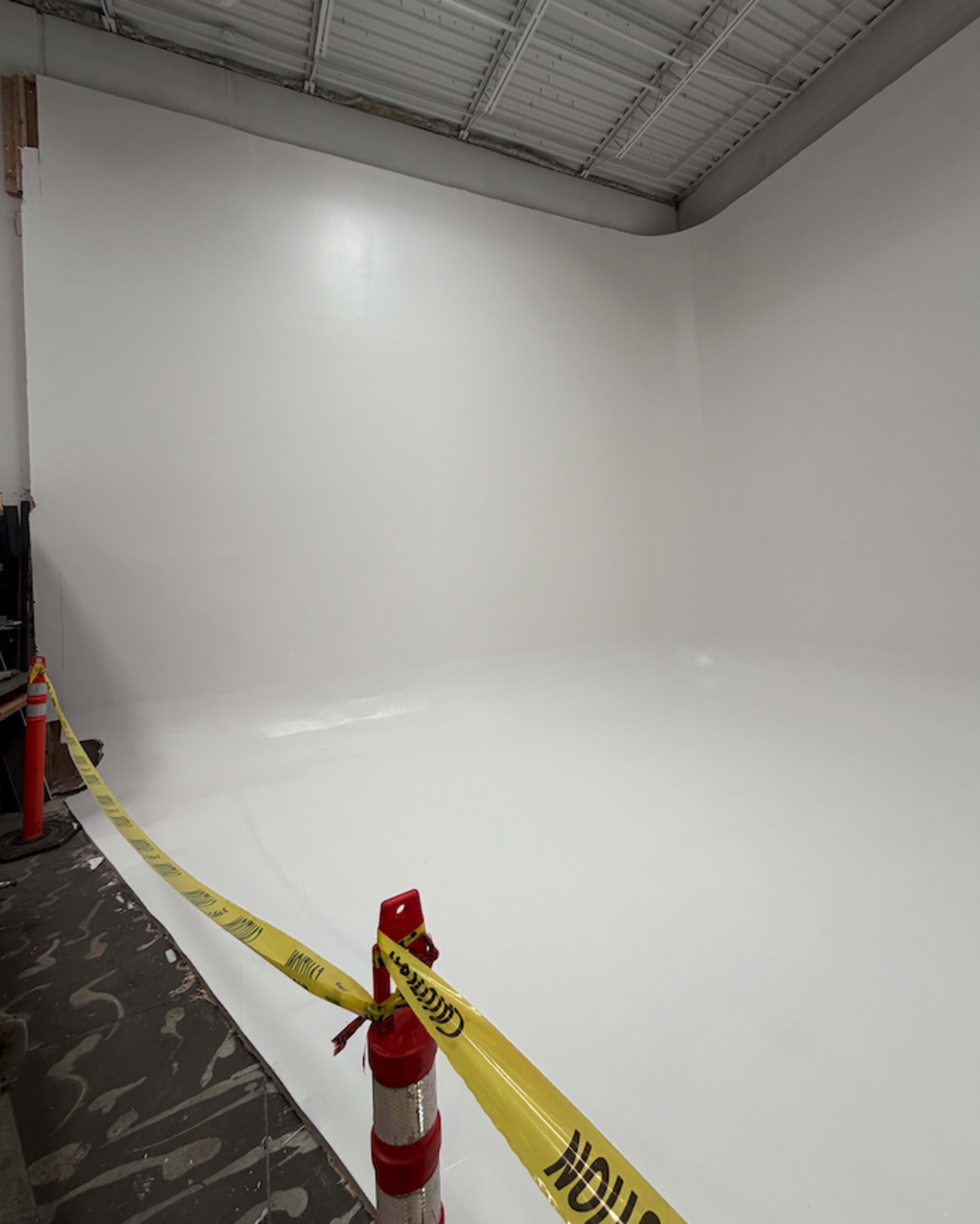 A large, empty room with white walls and a shiny floor is cordoned off with yellow caution tape.