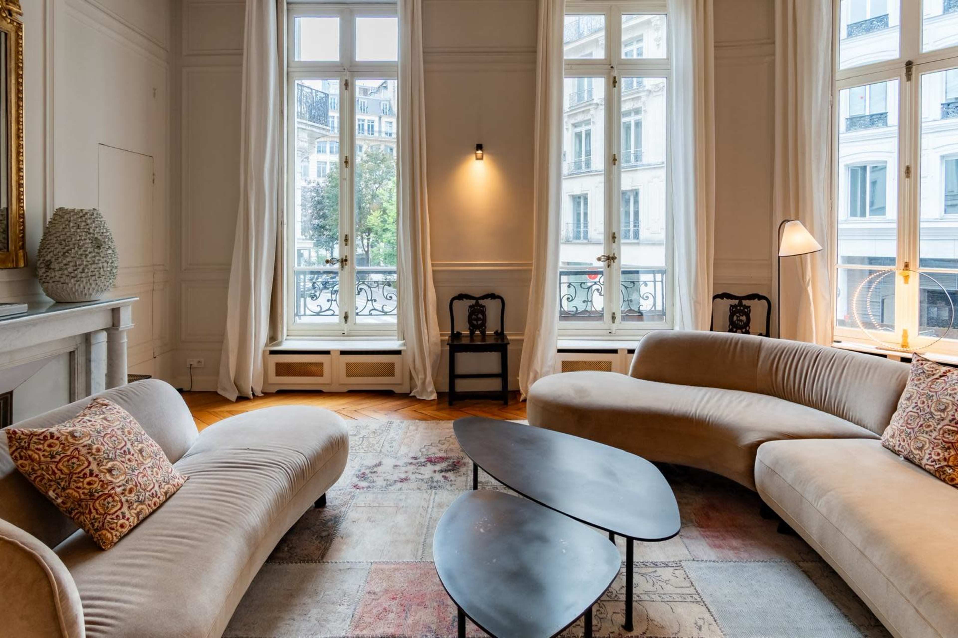 The image features a modern living room with a curved sofa, a low coffee table, and large windows that let in natural light.