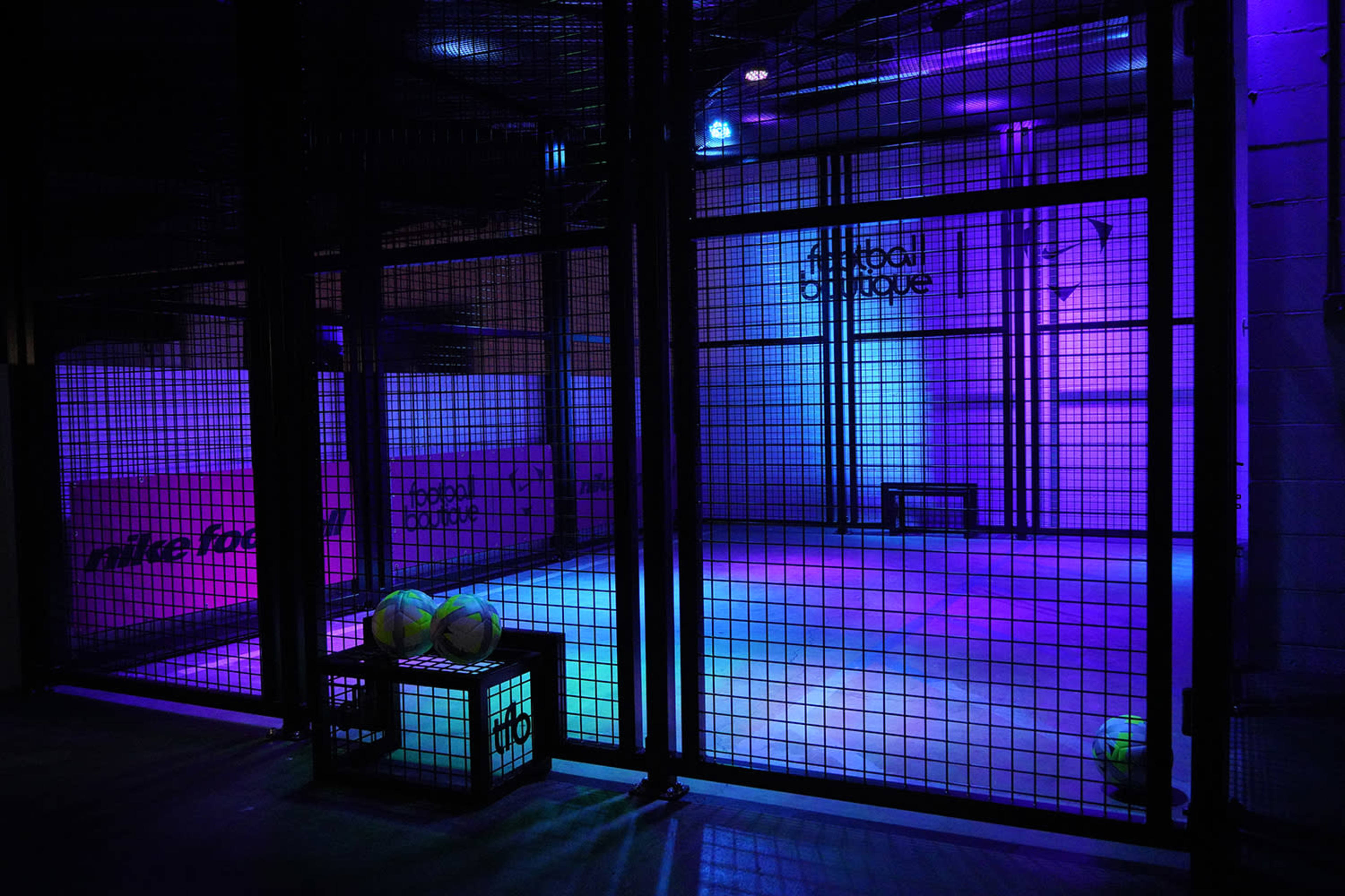 The image shows a brightly lit indoor court surrounded by a metal fence, featuring colorful purple and blue lighting.
