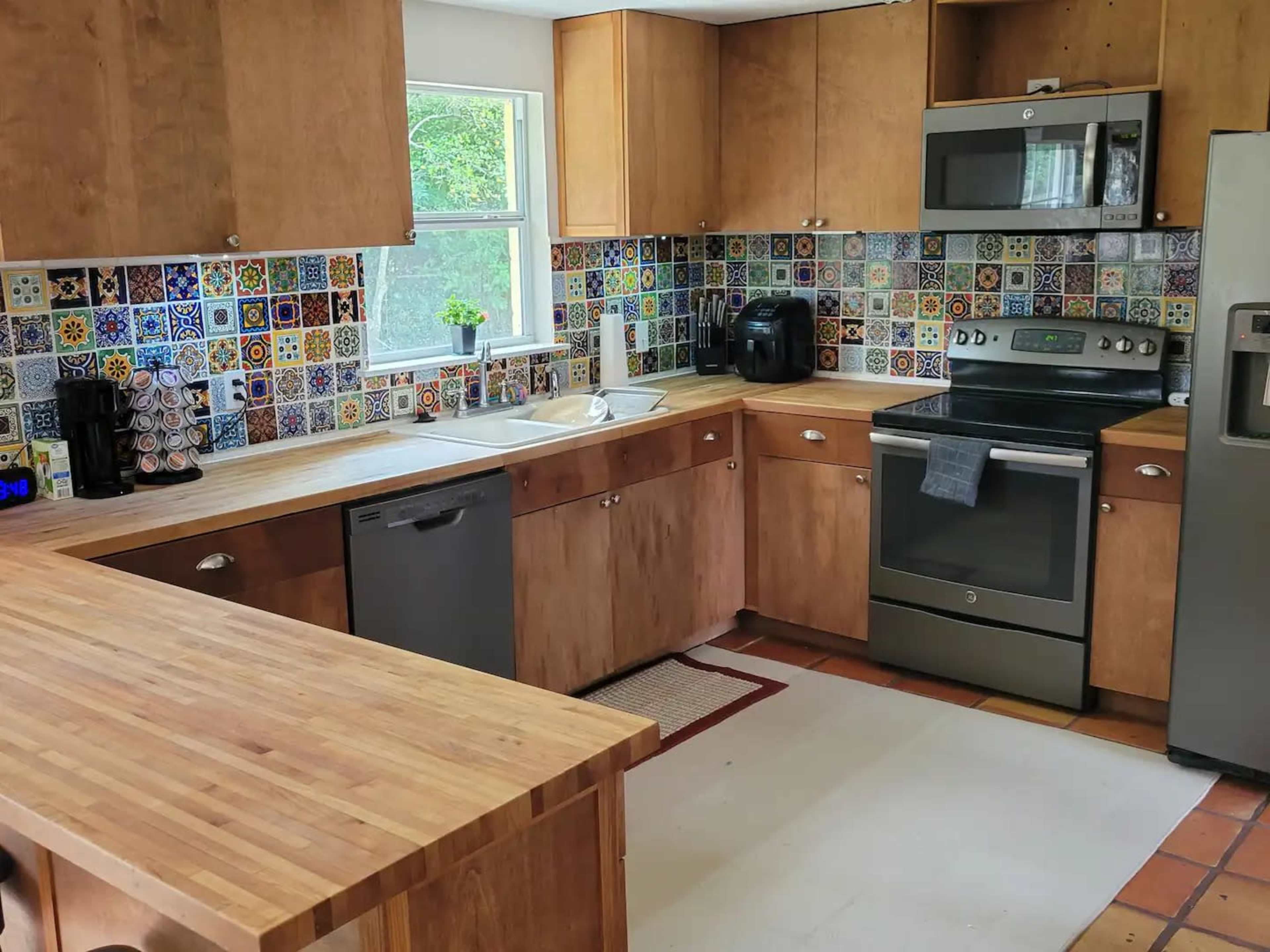 A kitchen with wooden cabinets, colorful tiled backsplash, stainless steel appliances, and a central wooden island.