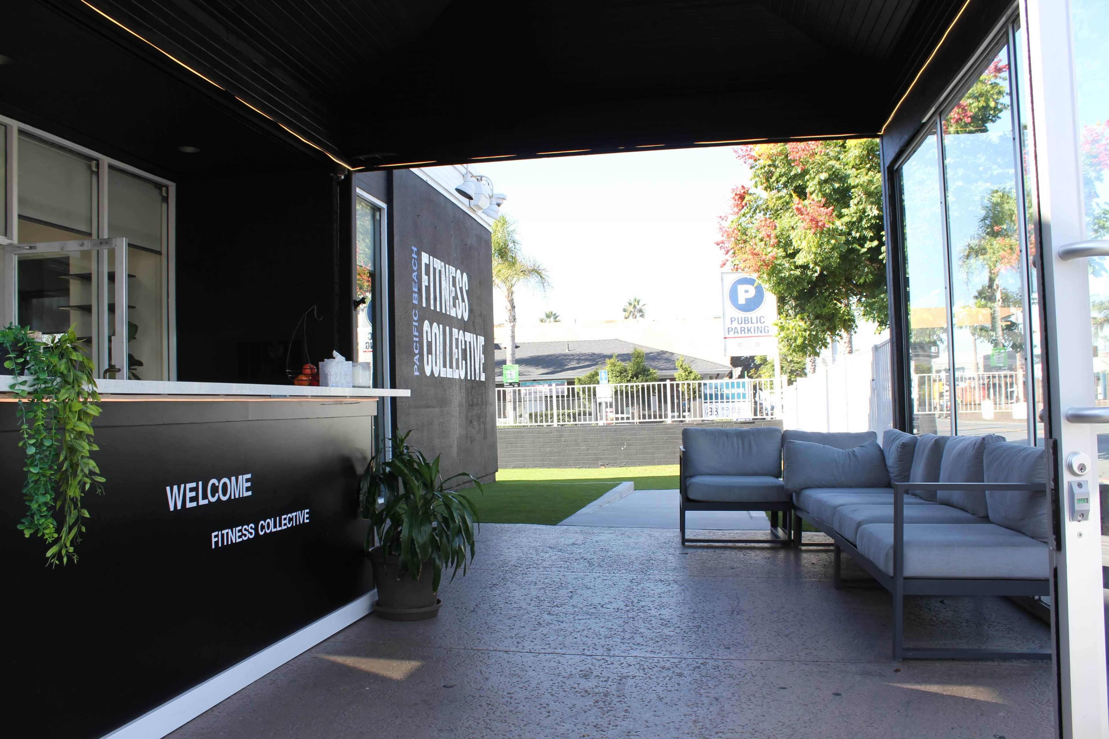 A modern fitness facility entrance with a reception area featuring a welcome sign and a seating area outside.