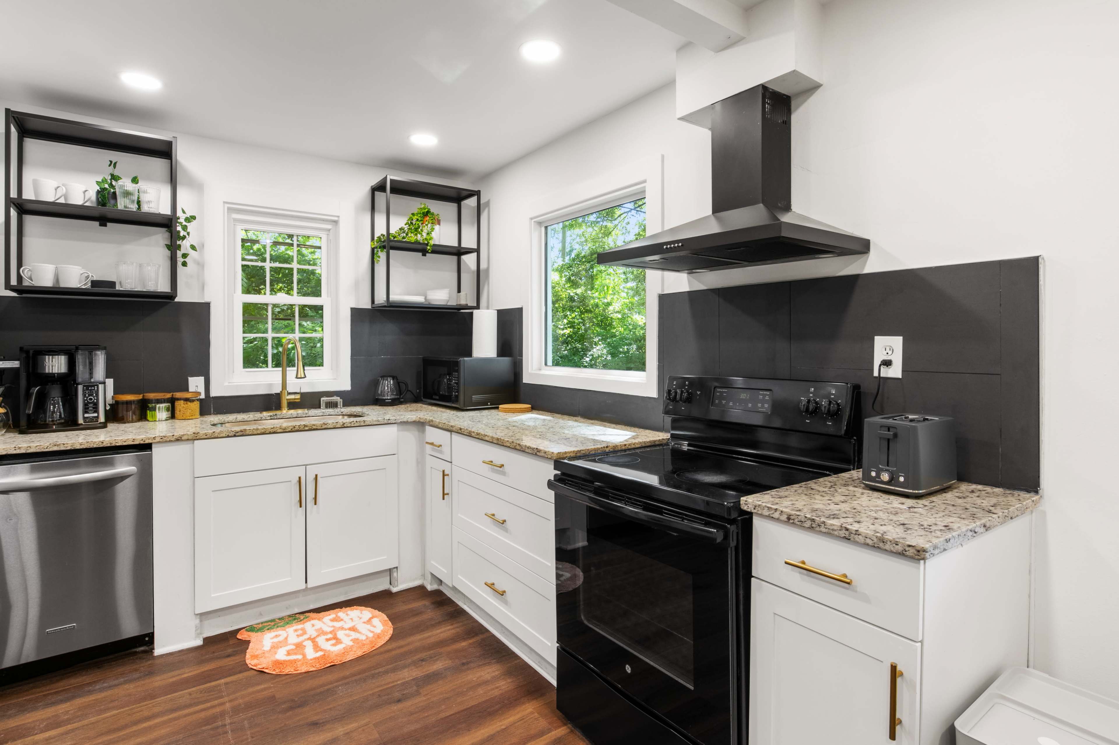 A modern kitchen with white cabinets, a black stove, and a stainless steel refrigerator, featuring a window that lets in natural light.