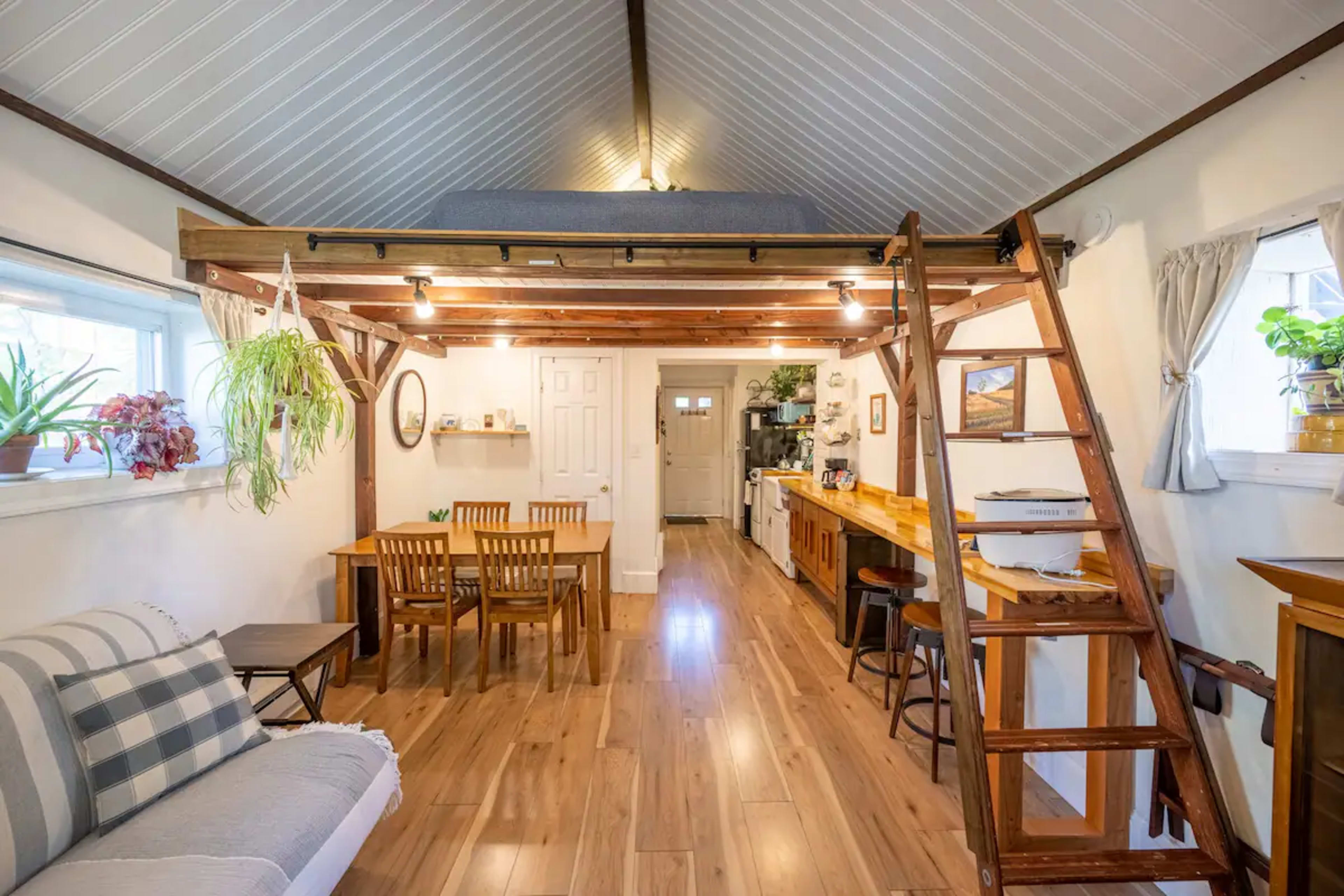 A small, open-concept living area featuring a wooden loft, a dining table, and a kitchen along one wall.