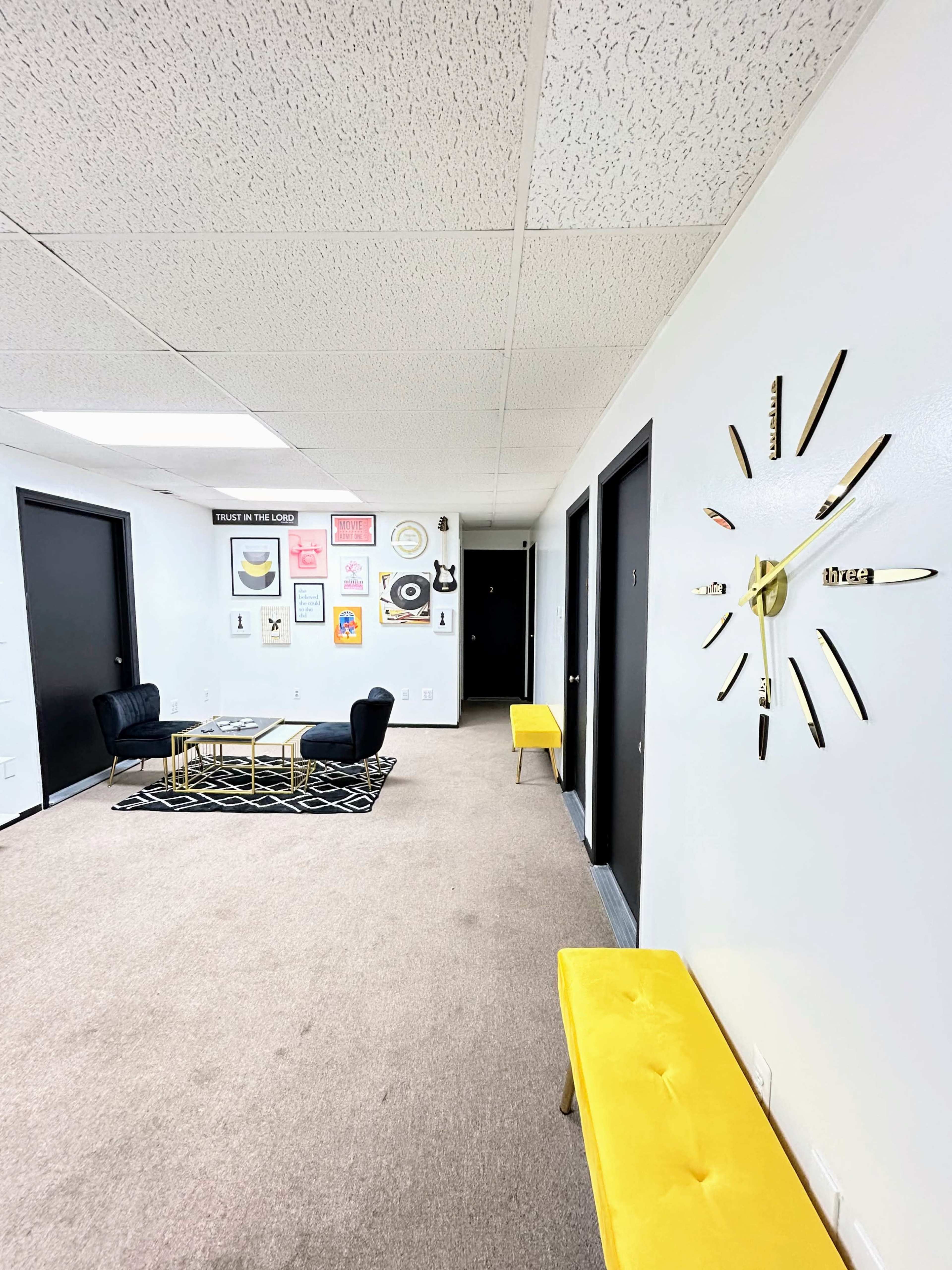 A hallway features a black and yellow color scheme with two seating areas, a modern clock, and various framed artworks on the walls.