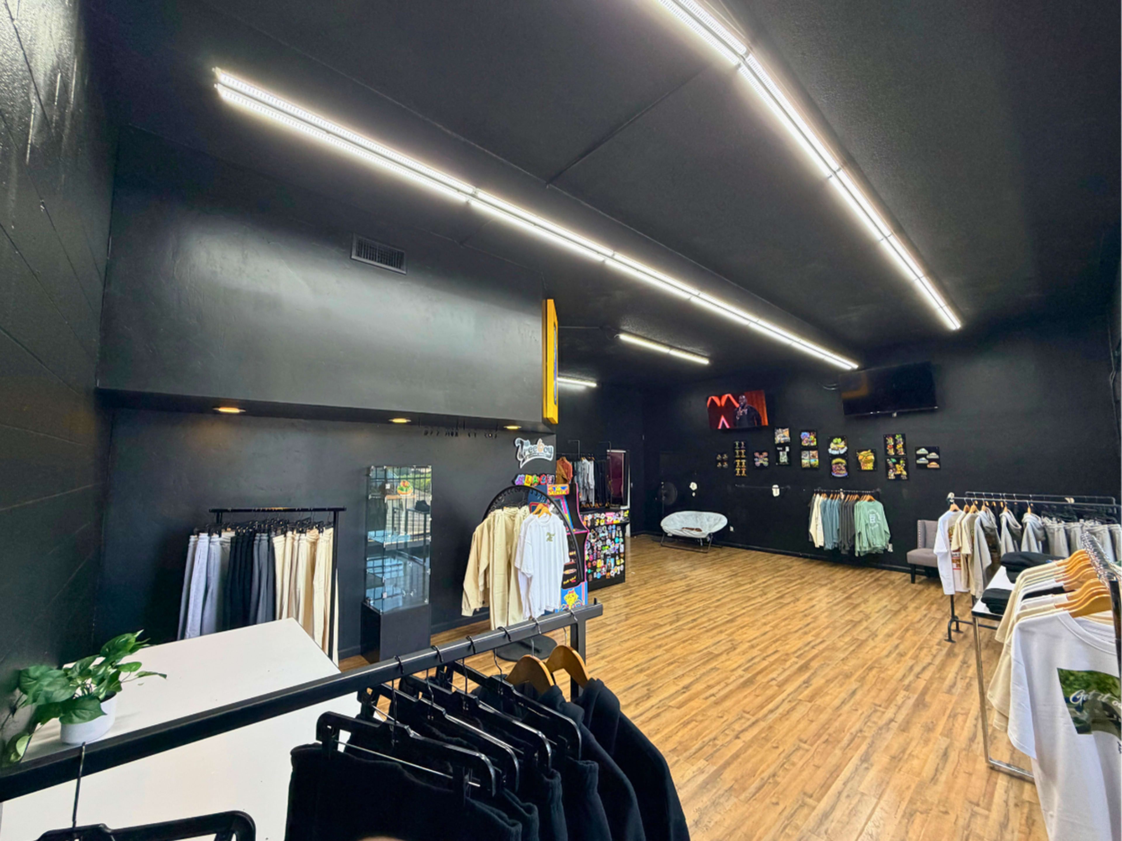 The image shows a clothing store interior with black walls, wooden flooring, and rows of hangers displaying various garments.