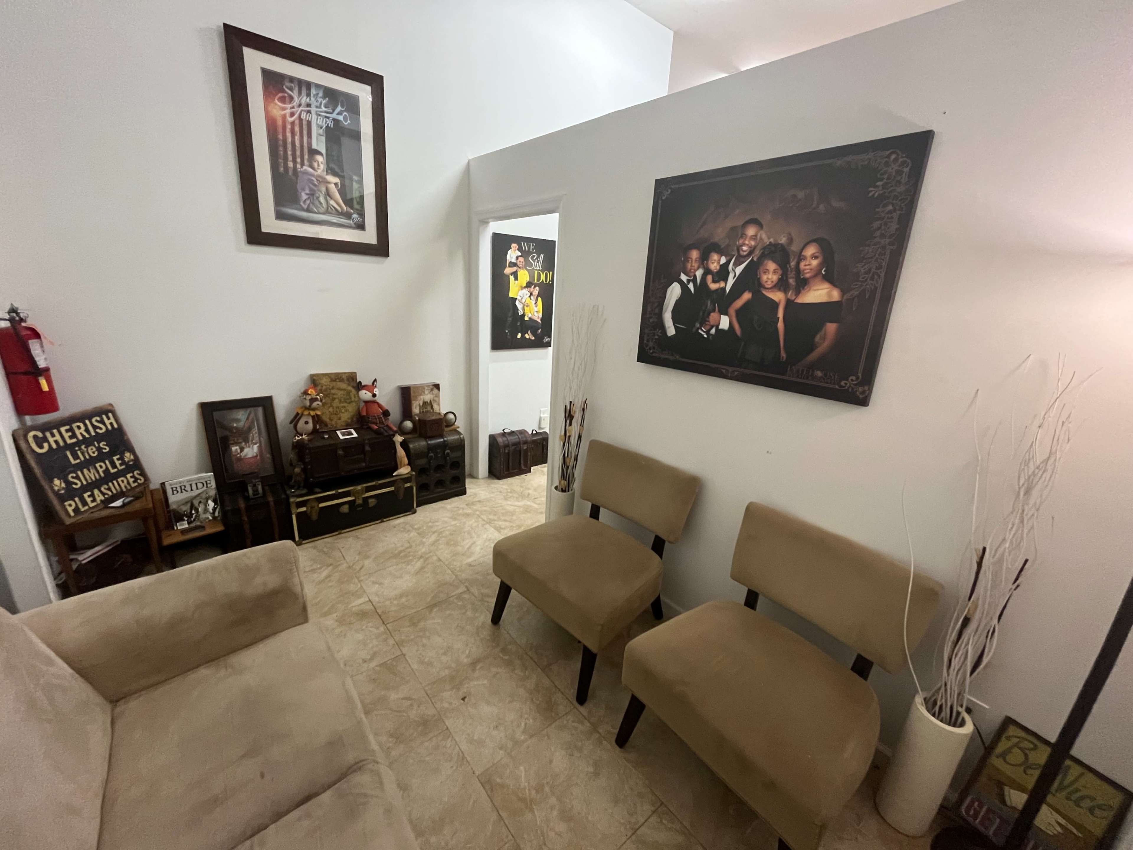 The room features a beige sofa, two chairs, a framed family portrait, decorative items, and a fire extinguisher on the wall.