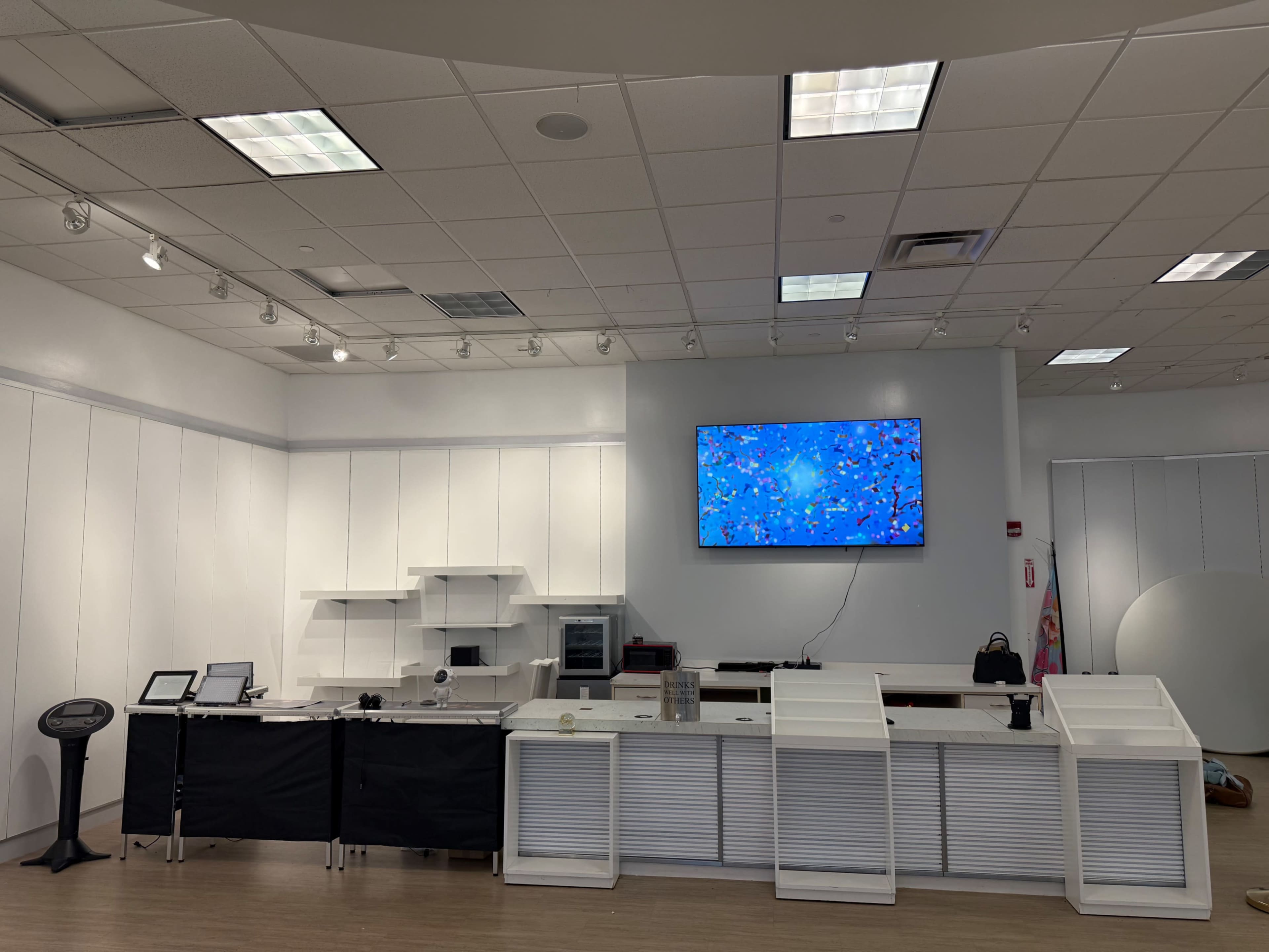 The image shows a modern, minimalist retail space with a large screen on the wall and a seating area along one side.