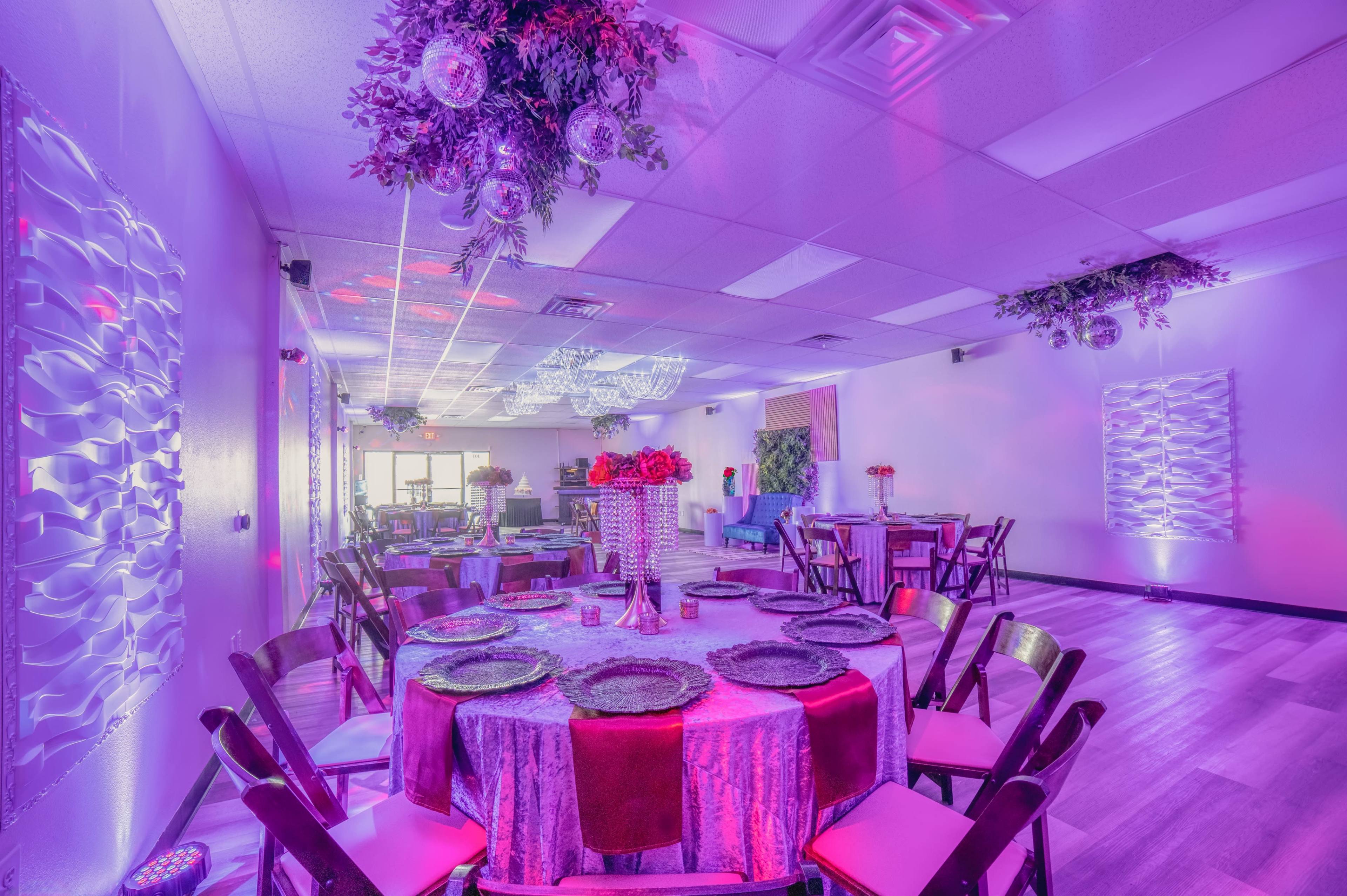 A brightly lit event space features round tables set with colorful tableware and floral arrangements under decorative lighting.