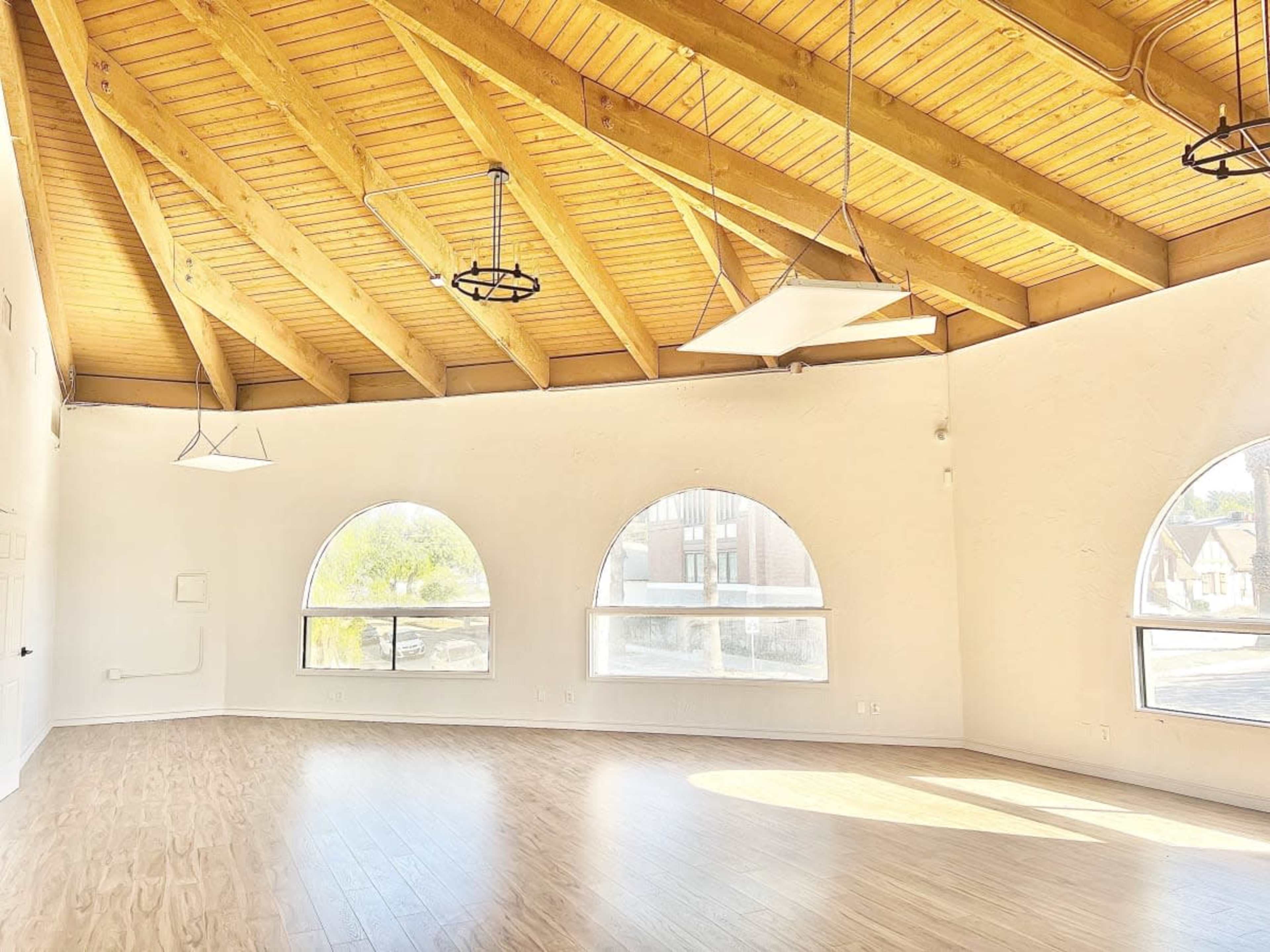 A spacious room with a high, wooden beam ceiling and large arched windows that let in natural light.