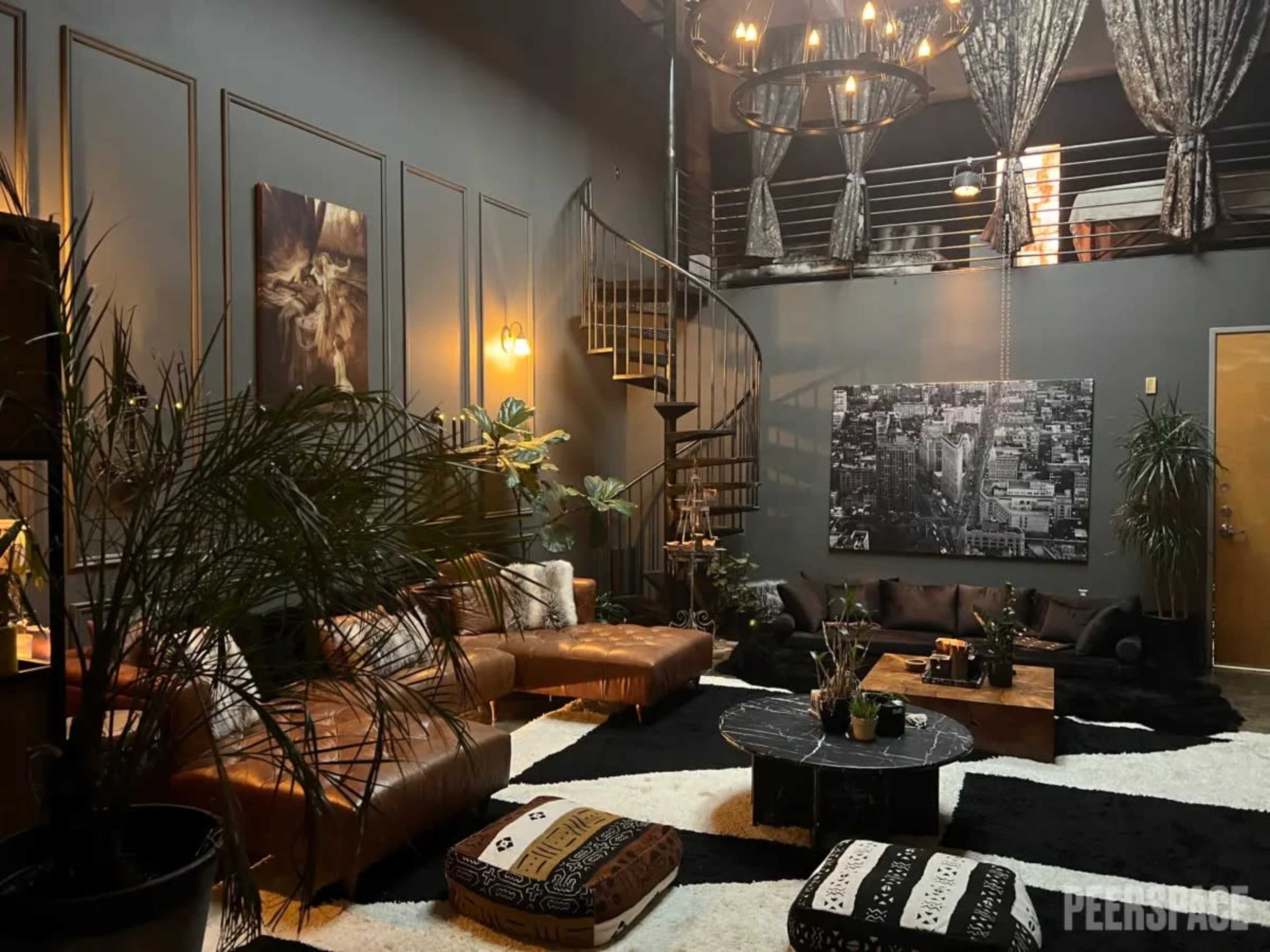 A stylish living area with a spiral staircase, leather sofas, a large black and white photograph on the wall, and decorative plants.