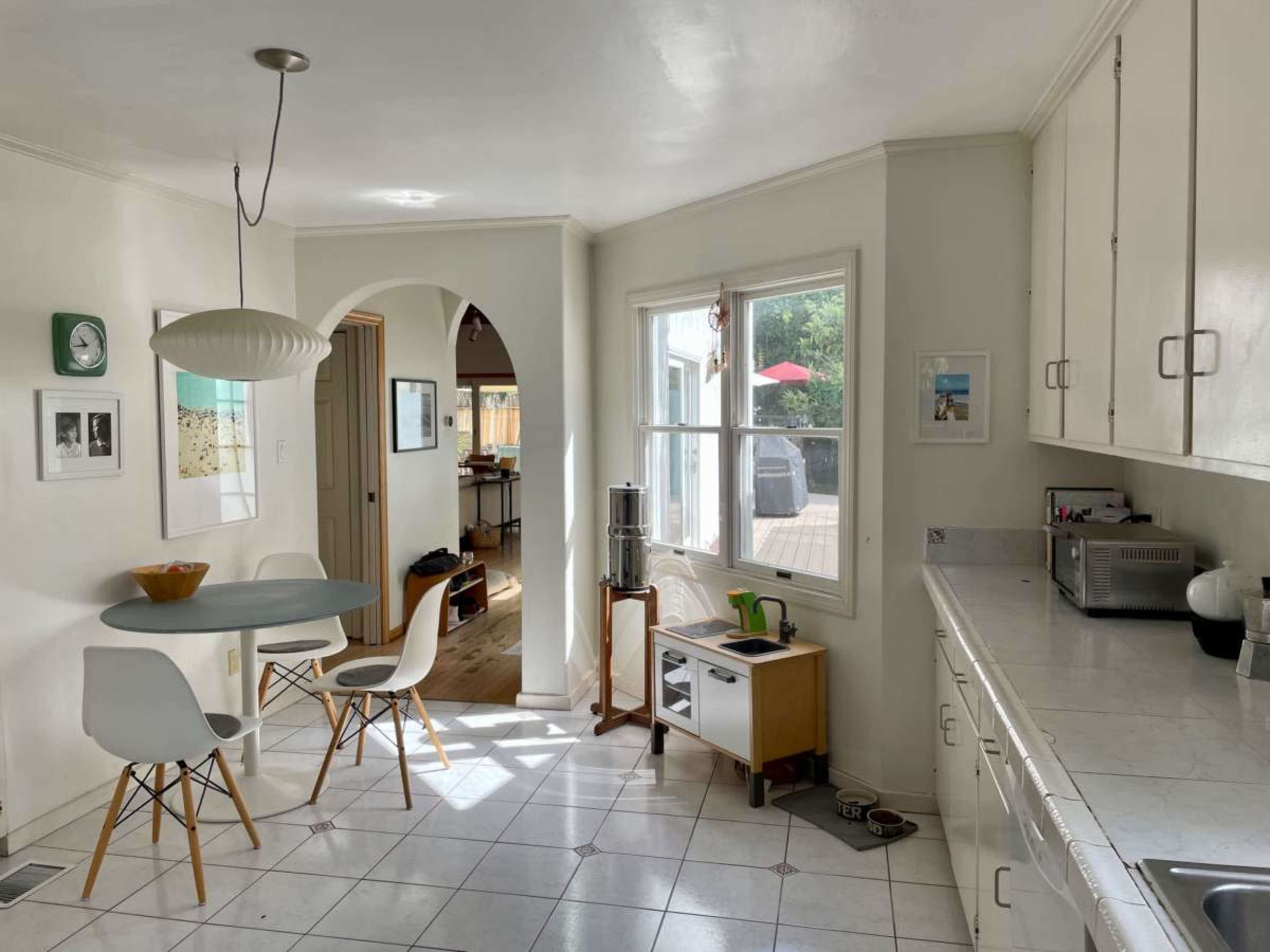 A compact kitchen features a round dining table with four chairs, a window offering natural light, and a small bar area with kitchen appliances and decor.