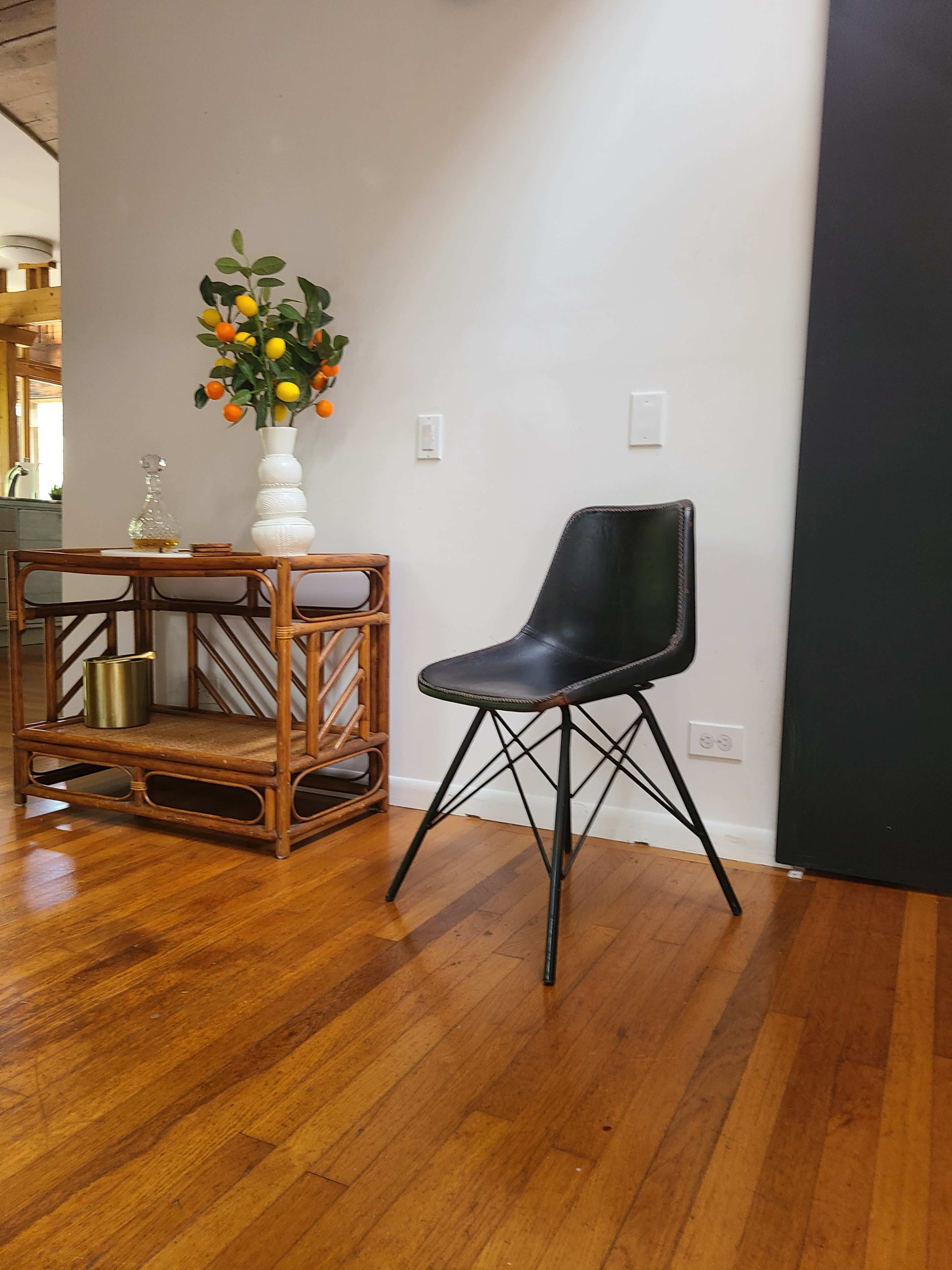 A black chair with metal legs stands next to a wooden console table adorned with a vase and artificial fruit.