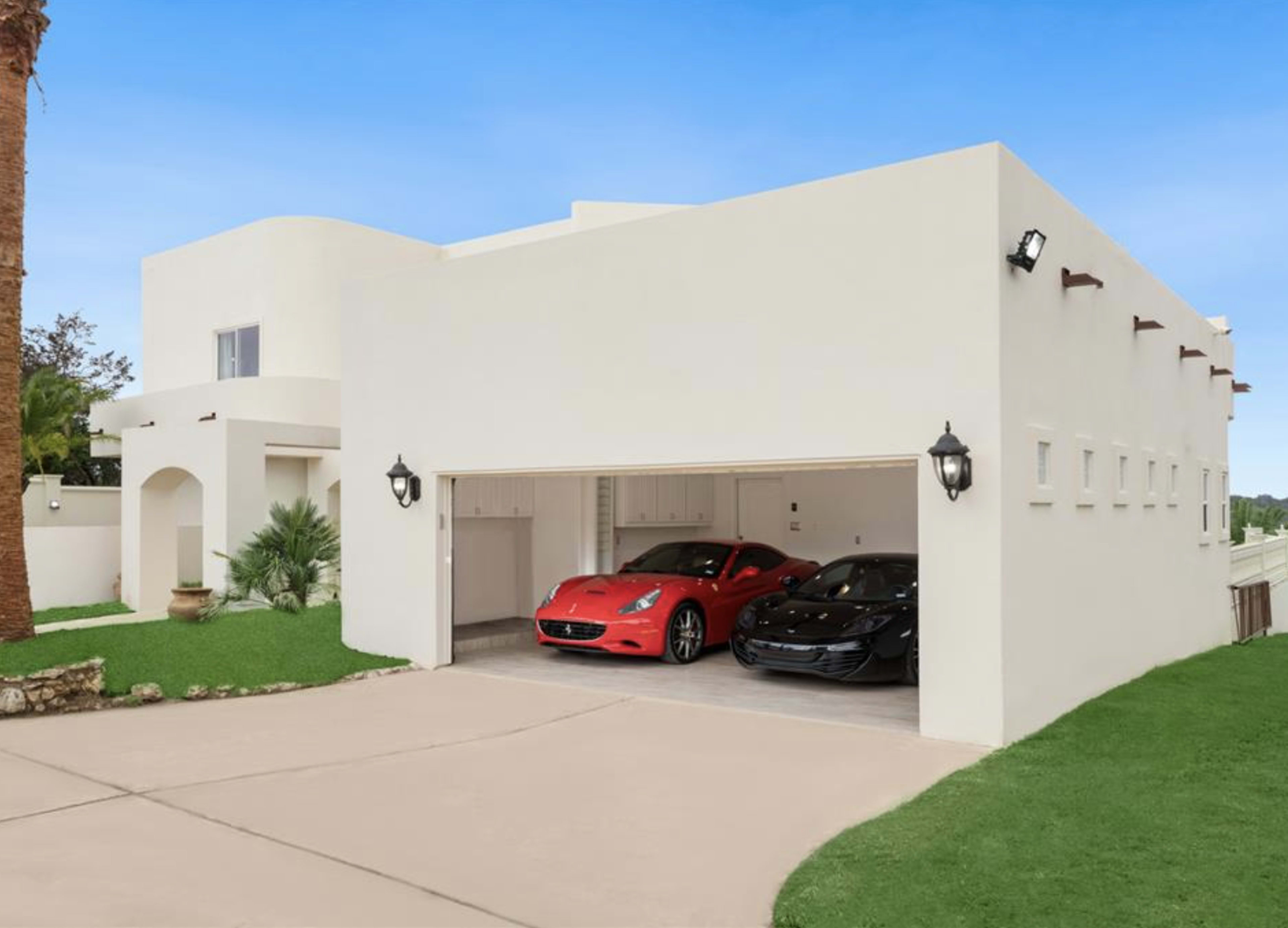 A modern white house with a two-car garage containing a red sports car and a black sports car.