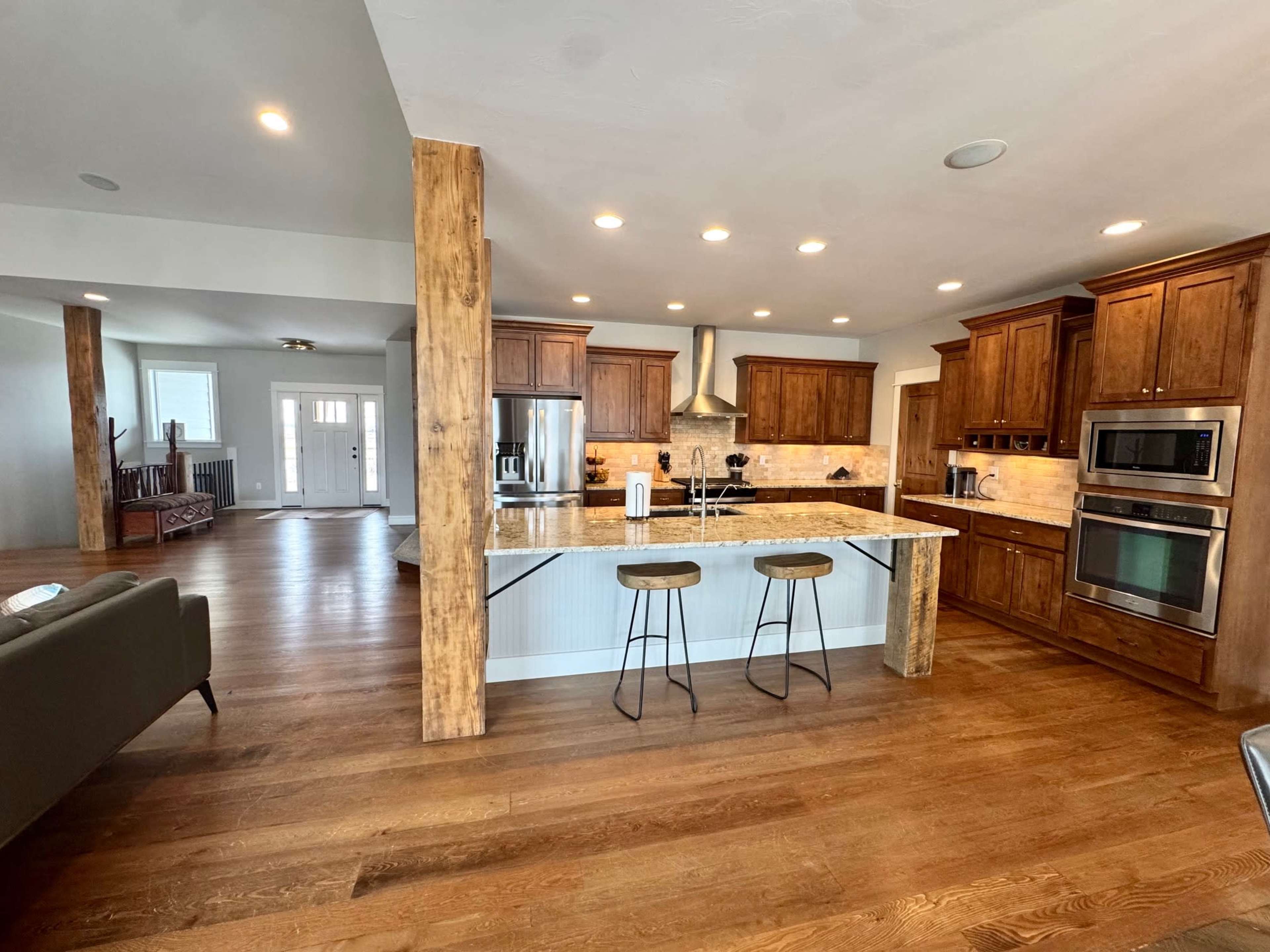 A modern kitchen features wooden cabinetry, a central island with bar stools, and stainless steel appliances against a backdrop of hardwood flooring.