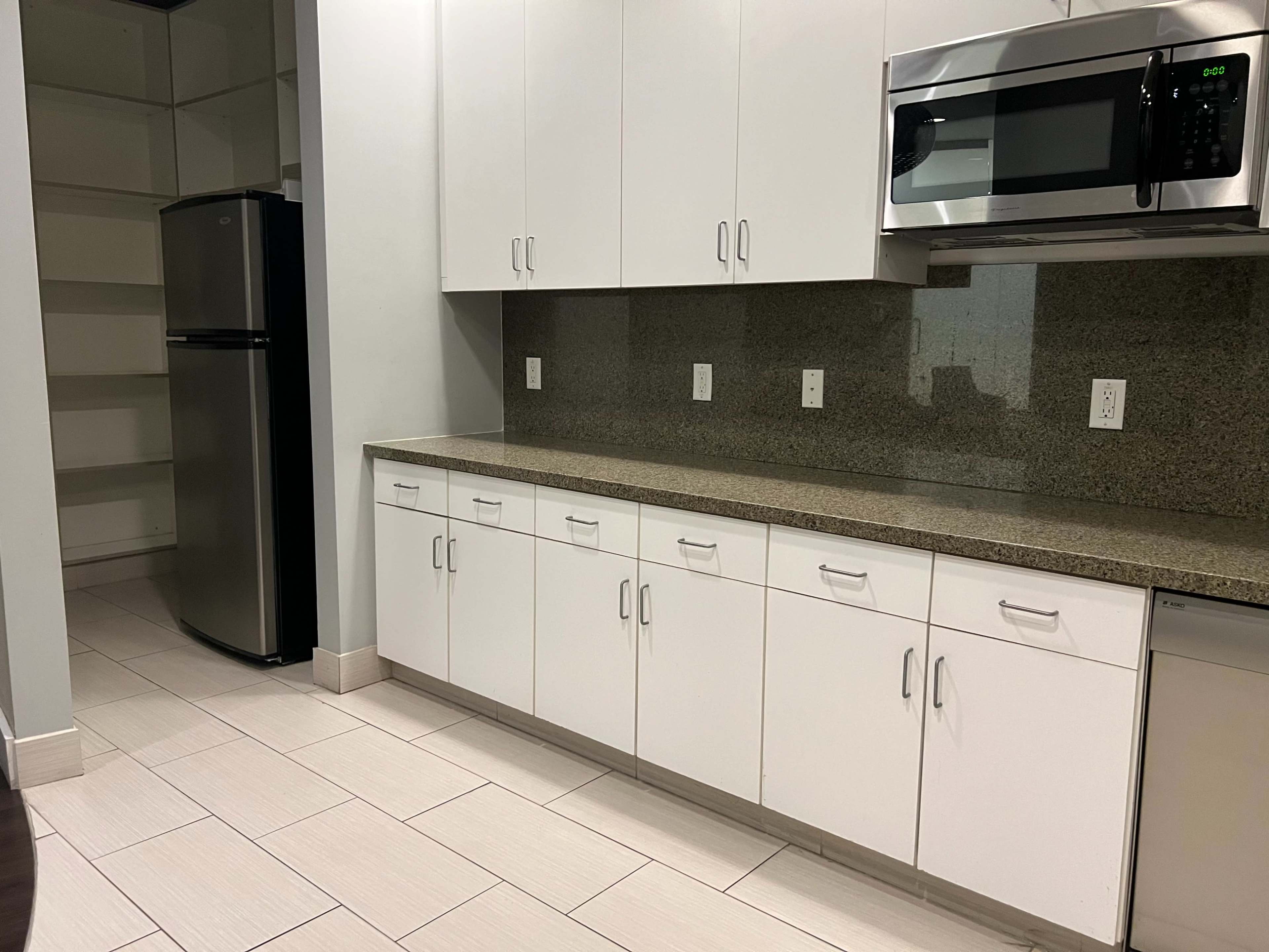 A modern kitchen with white cabinetry, a stainless steel microwave, and a black refrigerator against a green speckled granite countertop.