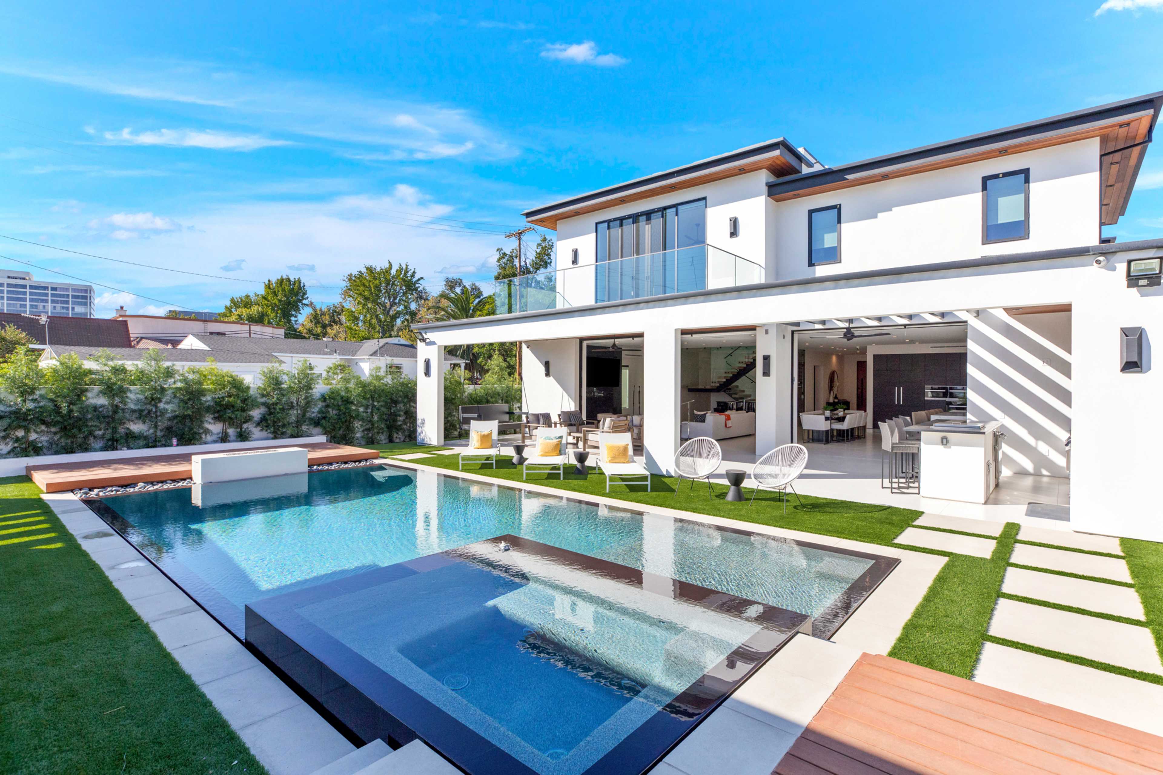 A modern two-story house with a swimming pool and outdoor seating area surrounded by a landscaped yard.