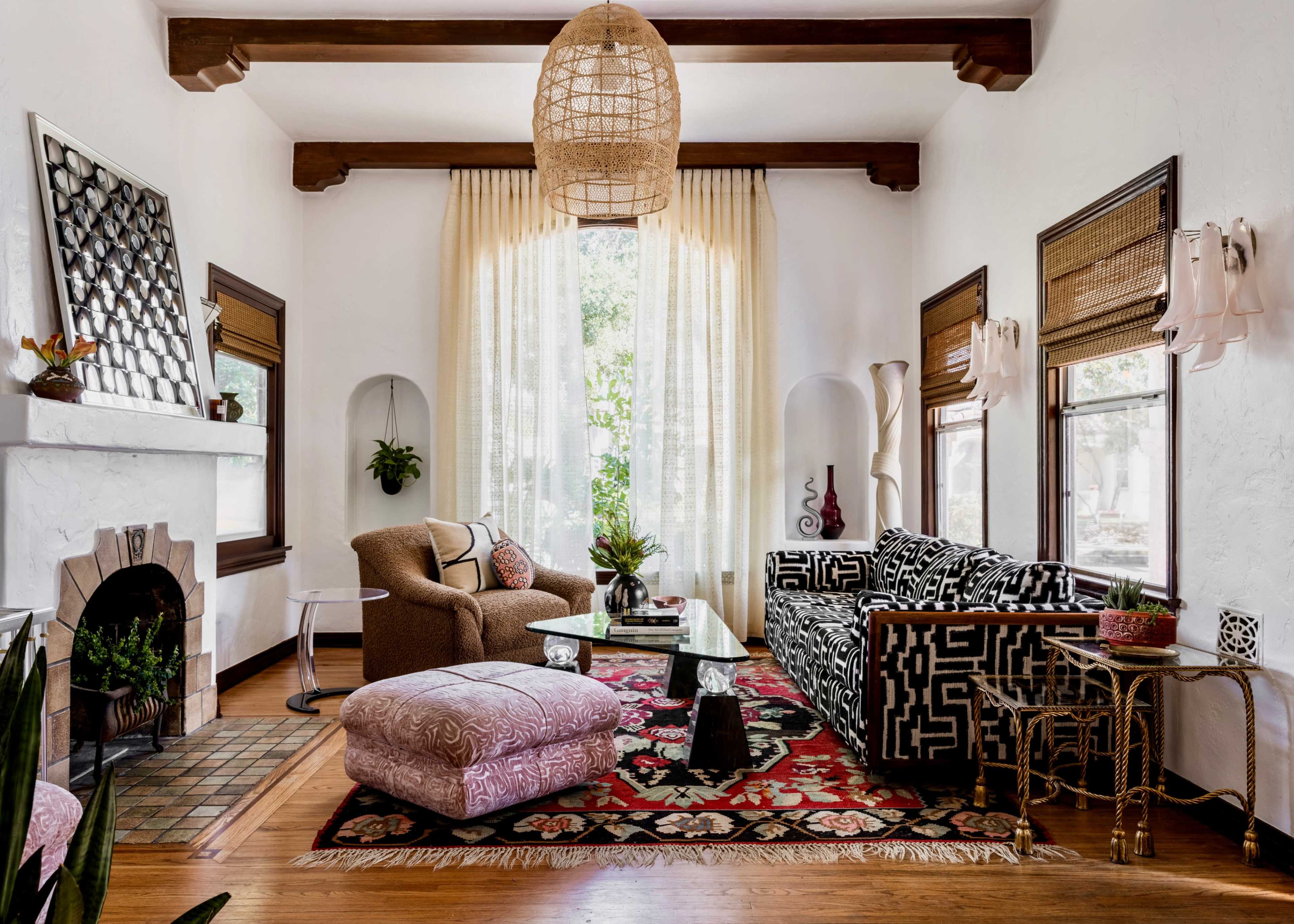 The scene depicts a cozy living room with a patterned black and white sofa, a relaxed chair, a coffee table, and an area rug, all complemented by large windows and light-colored drapes.