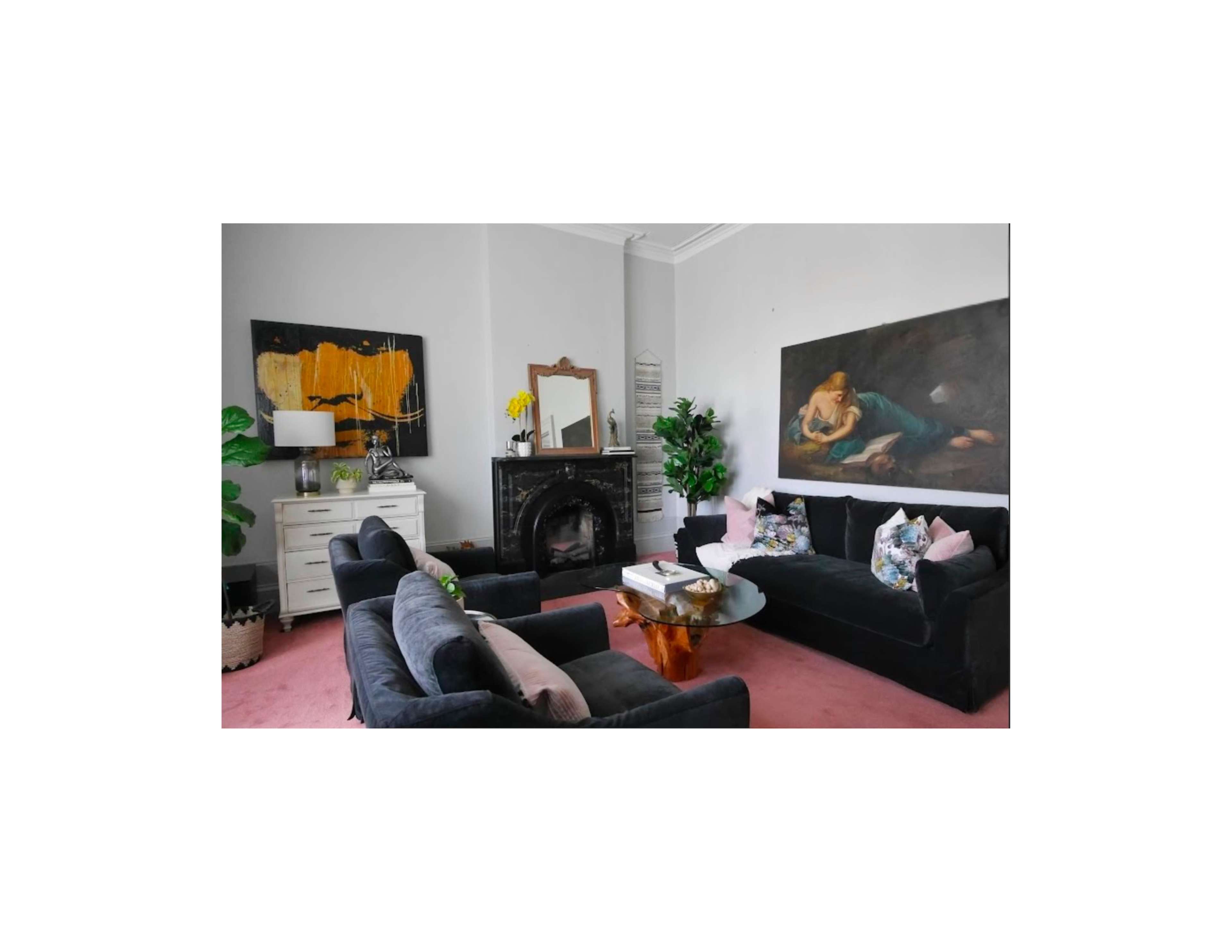 The image shows a living room featuring two dark sofas, a coffee table, a fireplace, and artwork on the walls.