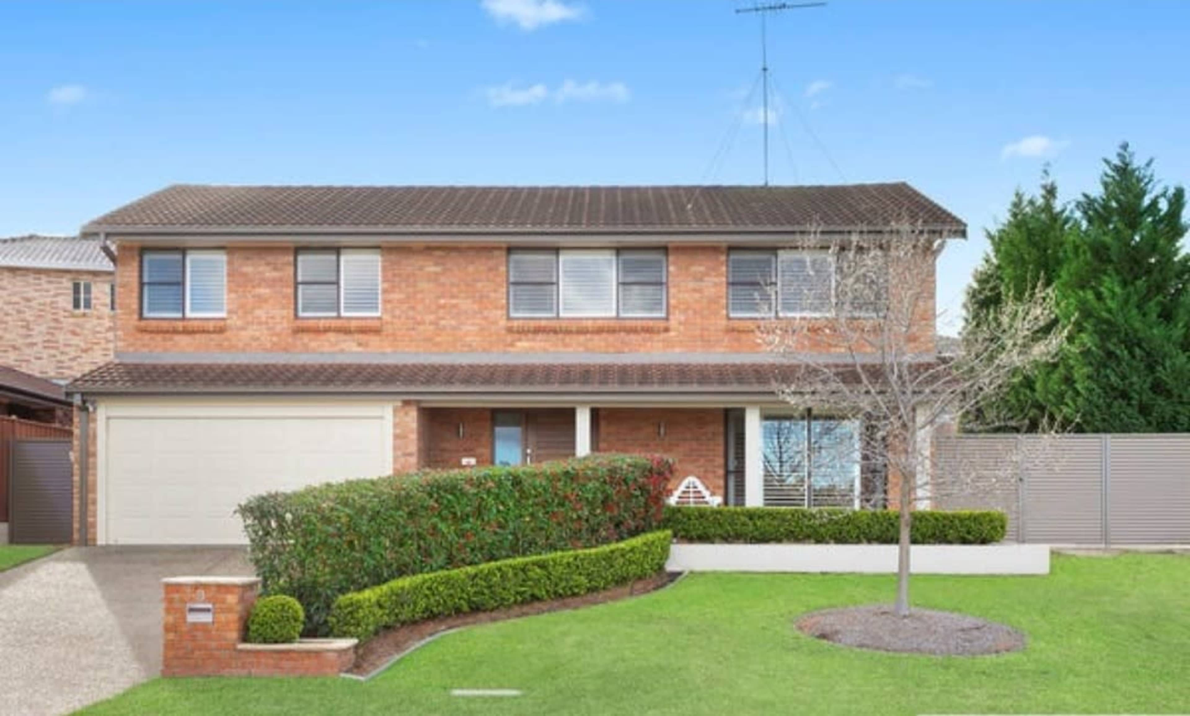 The image shows a two-story brick house with a neatly landscaped front yard and a paved driveway.