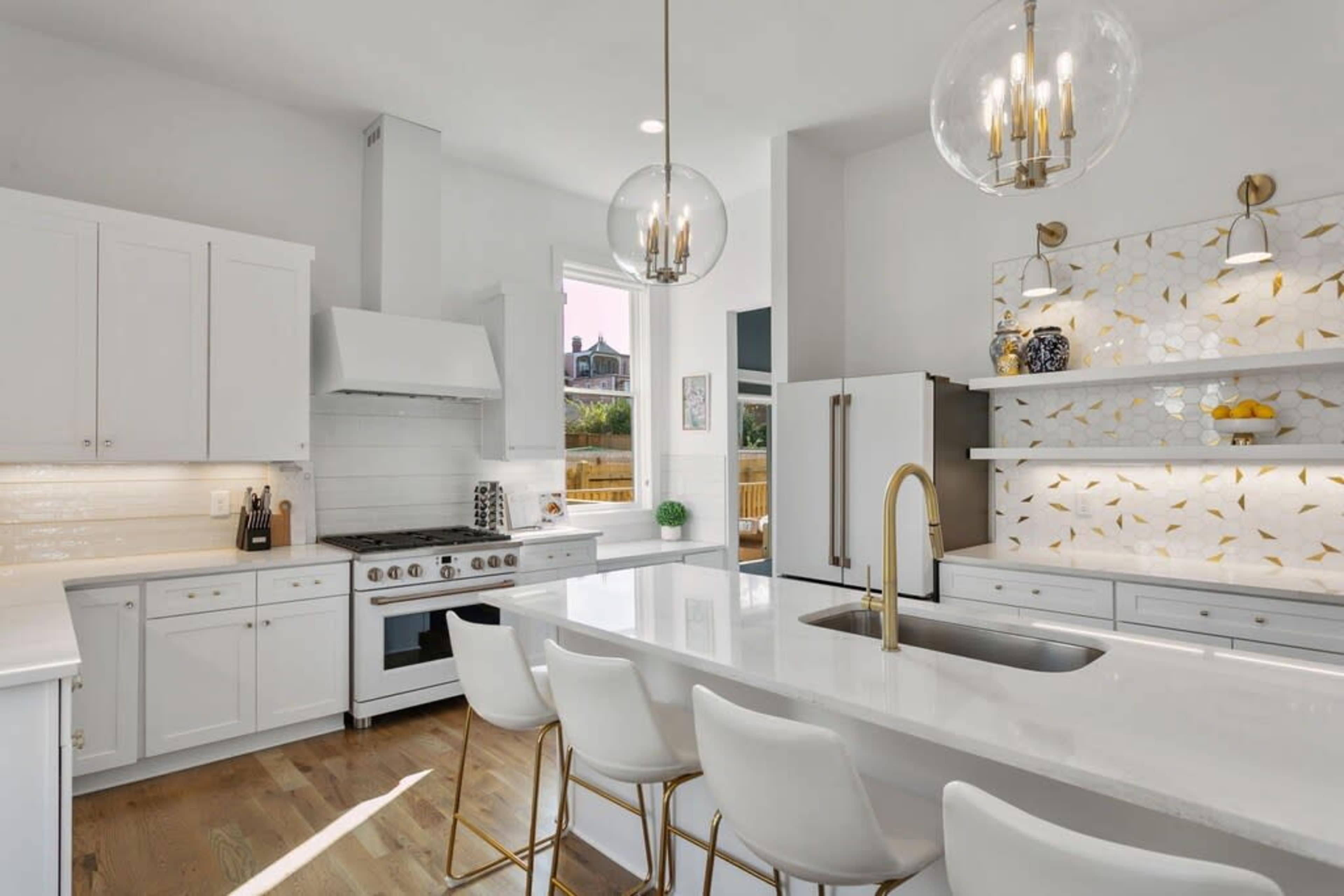 A modern kitchen features white cabinetry, a large island with four bar stools, and decorative wall tiles.
