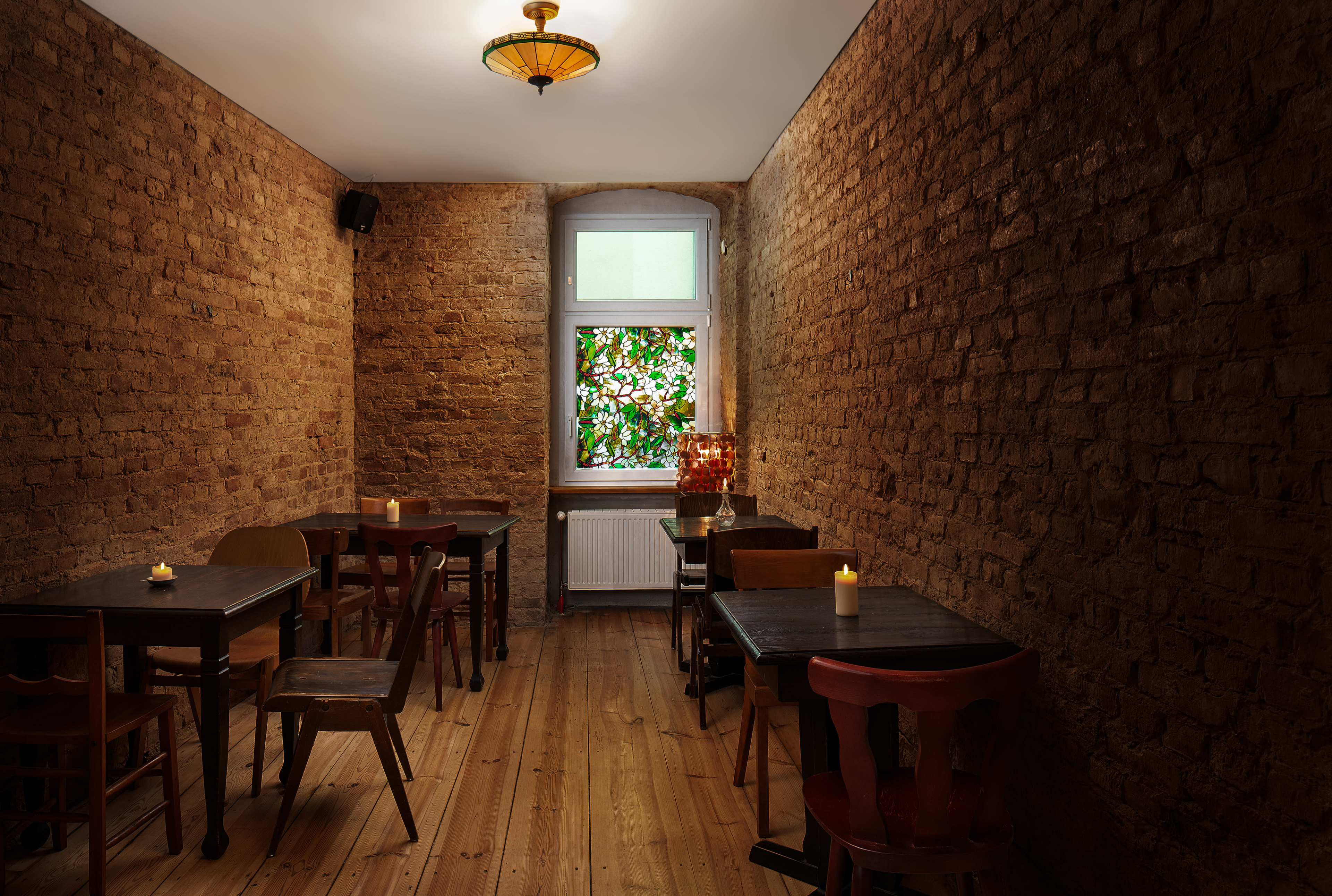A small cafe features wooden tables and chairs, exposed brick walls, and a stained glass window illuminating the space.