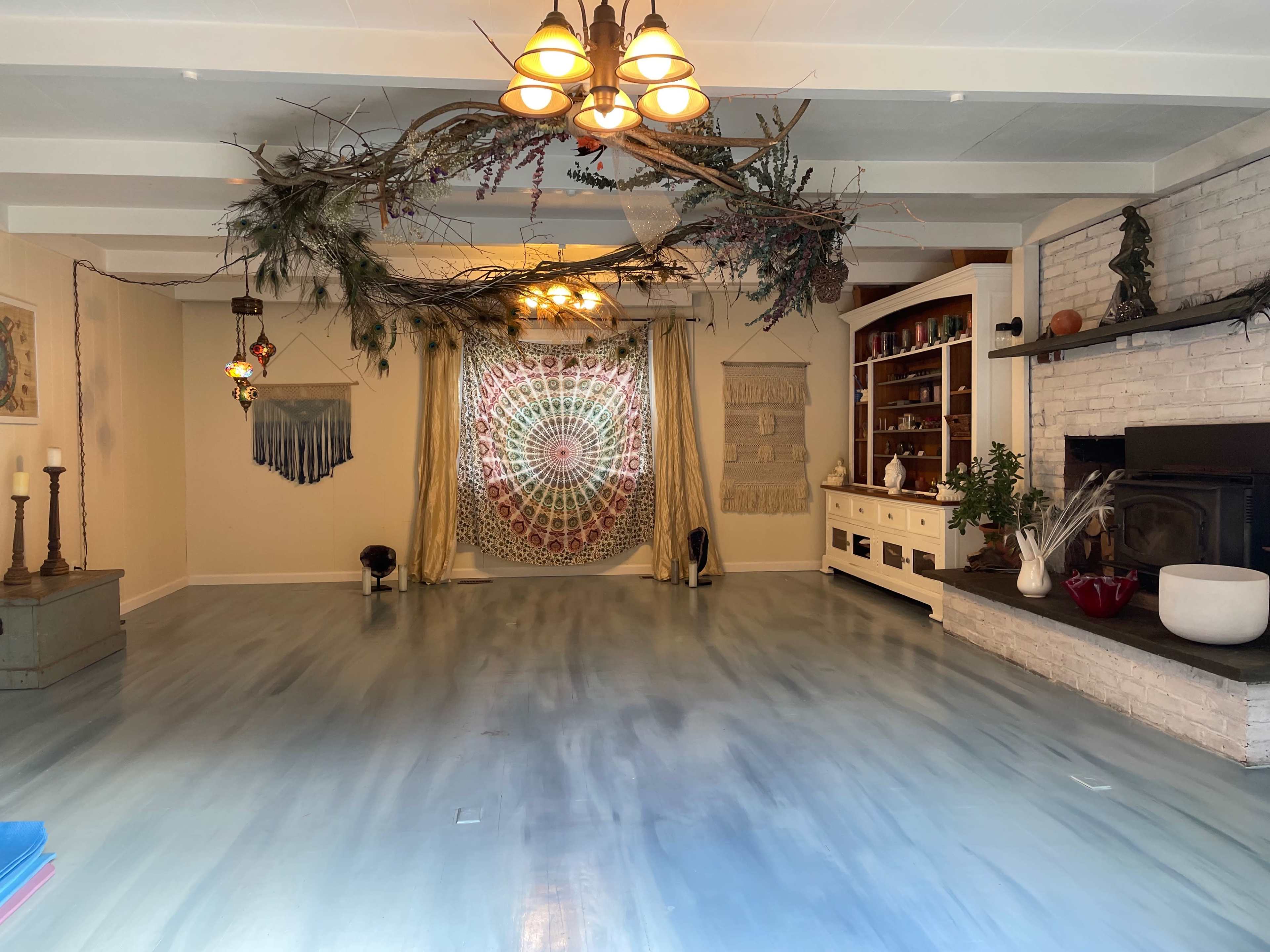 The spacious room features a patterned wall hanging, a rustic white-brick fireplace, and decorative elements suspended from the ceiling.