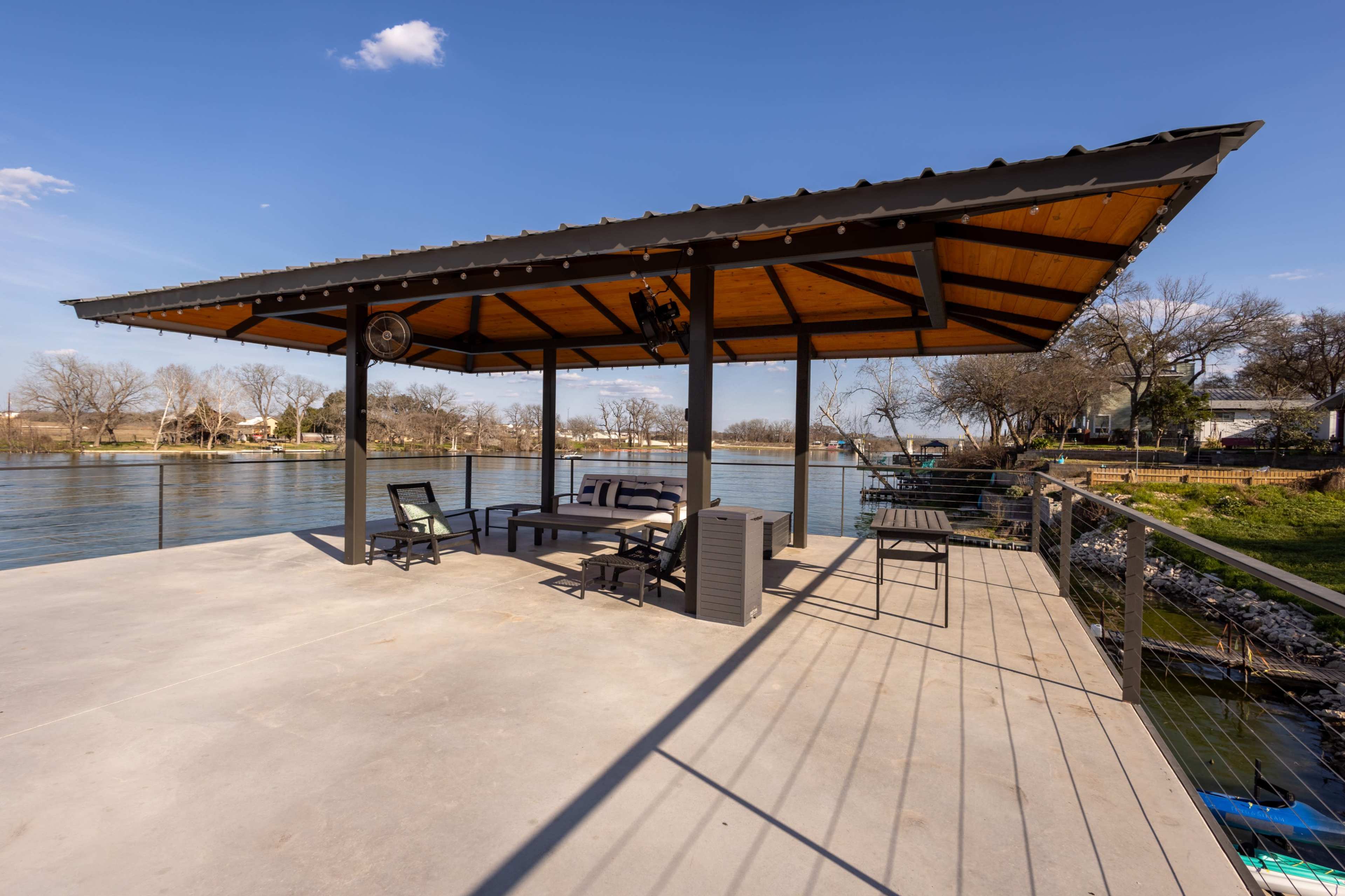 The image shows a covered dock with seating and a railing overlooking a calm river.