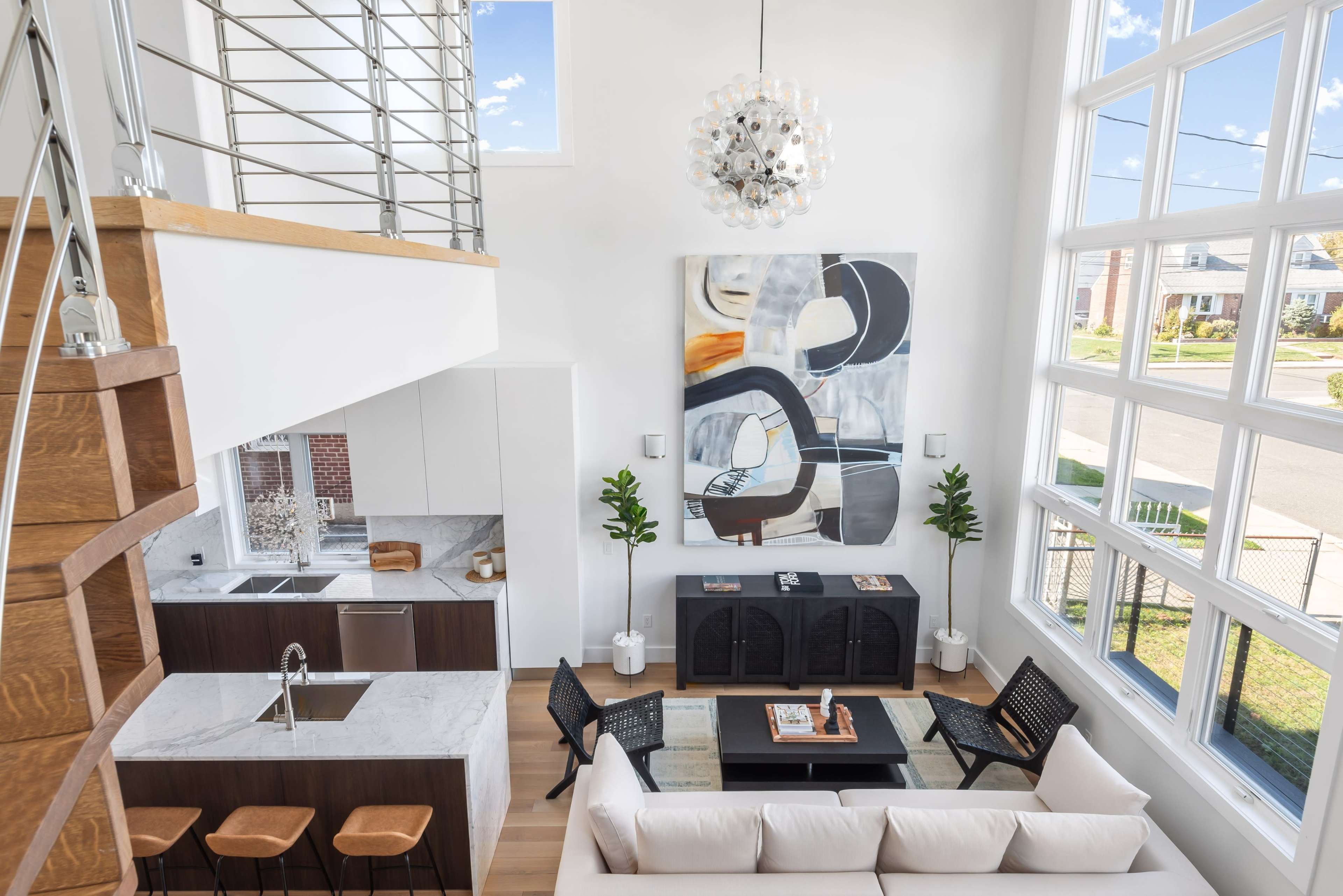 A modern living space with a high ceiling, large windows, a kitchen area, a sofa, and contemporary art on the wall.