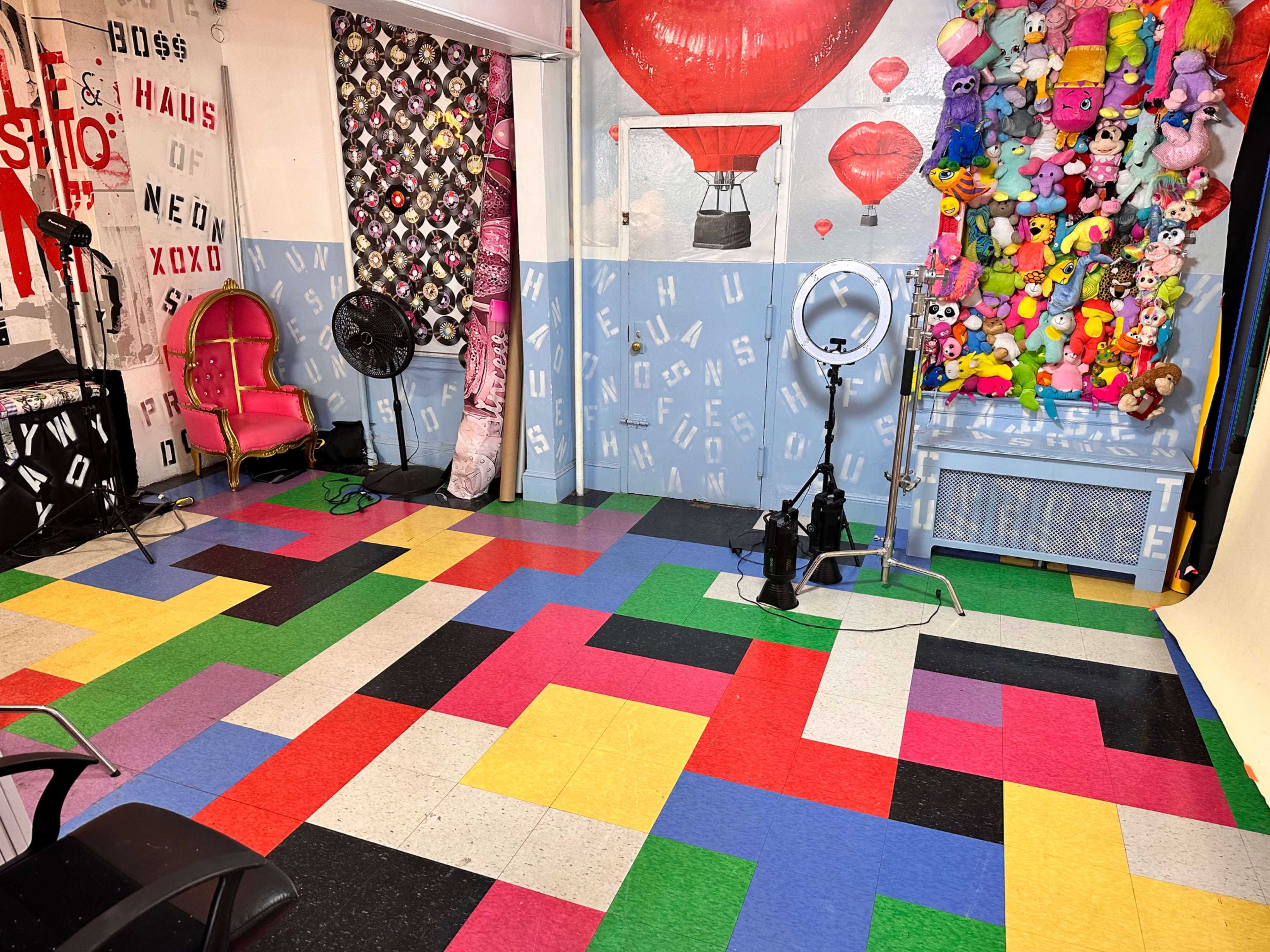 A colorful floor made of interlocking tiles in a studio setting, featuring a pink chair and a wall adorned with plush toys and various decorative elements.