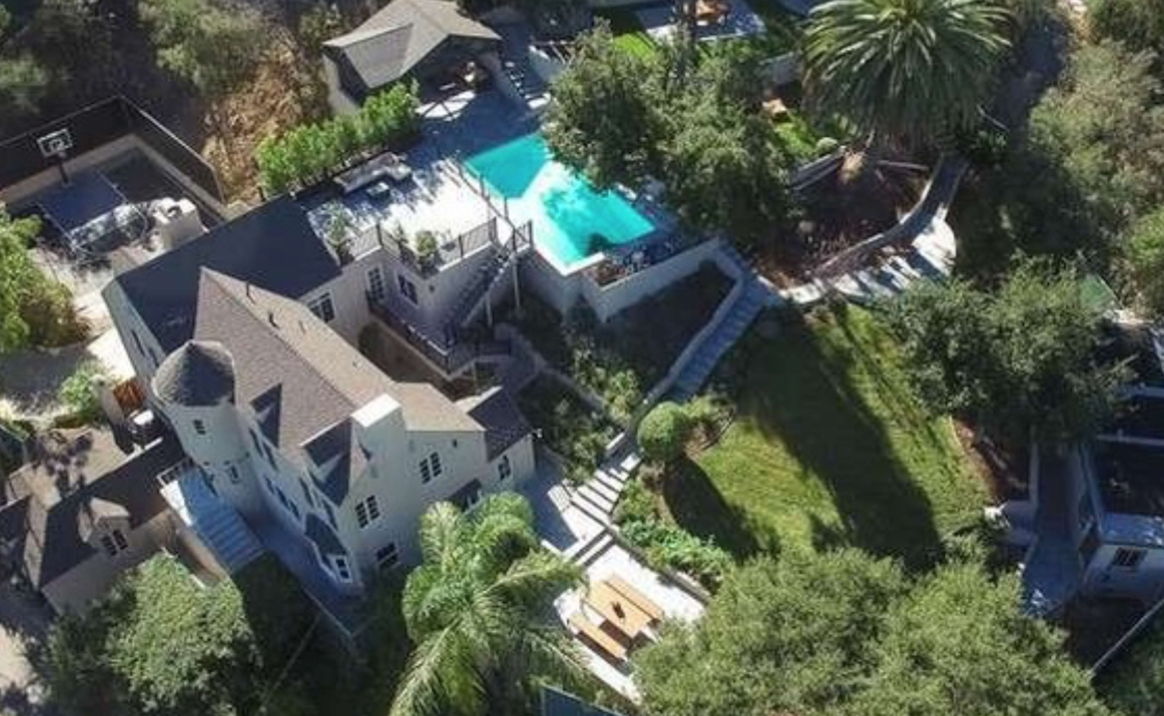 The image shows an aerial view of a large house with a pool, surrounded by trees and landscaped gardens.